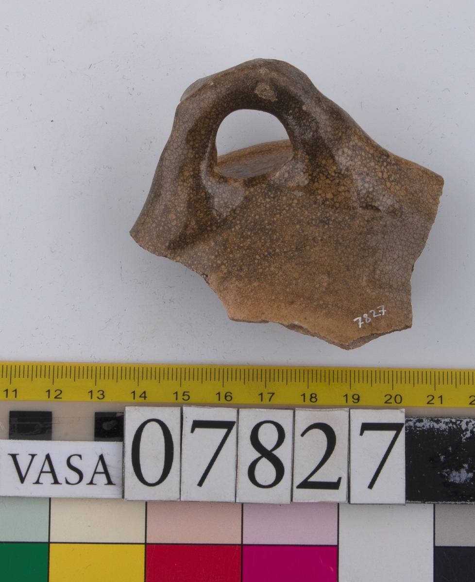 Del av skål.
1 st vertikal bandhänkel, tummad, 70 x 60 mm. Fragment av mynningsrand och buk. In- och utsida blyglaserad gulgrön.