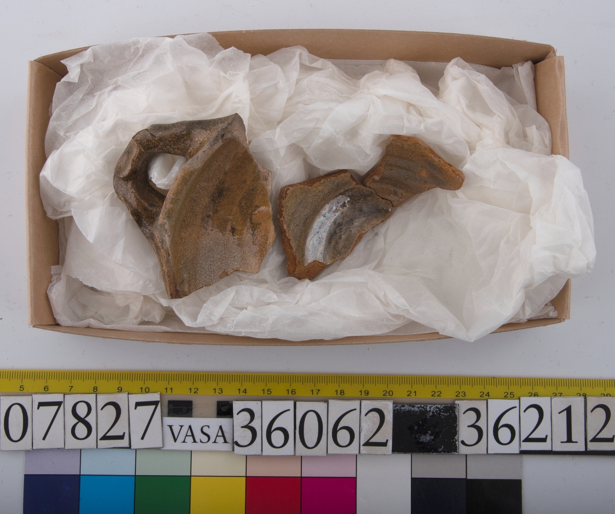 Del av skål.
1 st vertikal bandhänkel, tummad, 70 x 60 mm. Fragment av mynningsrand och buk. In- och utsida blyglaserad gulgrön.