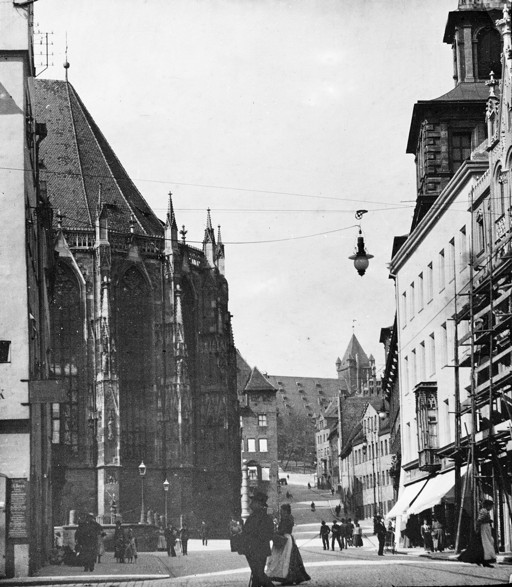 Skioptikonbild med motiv av gata vid Sankt Sebalduskirche i Nürnberg.
Bilden har förvarats i kartong märkt: Nürnberg 1901. VIII.. Text på bild: "Au Hauptmarkt"