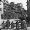 Skioptikonbild med motiv av kvinna med fyra små barn på gata i Nürnberg.
Bilden har förvarats i kartong märkt: Nürnberg VI. 1901