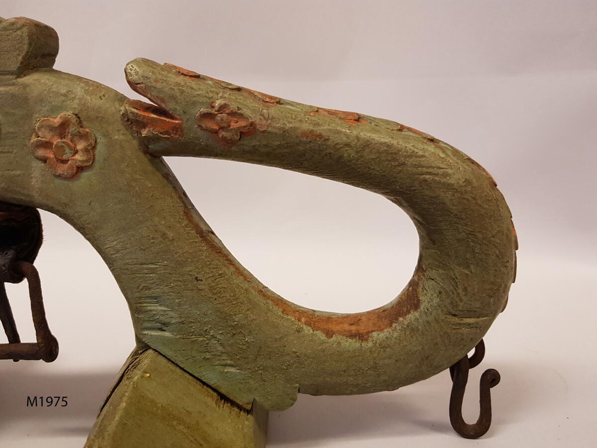 Selbåge, av björk. Målad i grönt och rött. Krönpartiet kronformigt. Ändarna i form av mot bågen tillbakaböjda ormhuvuden med ryggband av snidade hjärtan. På sidorna snidade blommor. Fasta selklackar utan stöd, fästade direkt på bågen. Järnkrampor med hakar för remtyget. Under bågen sölja.