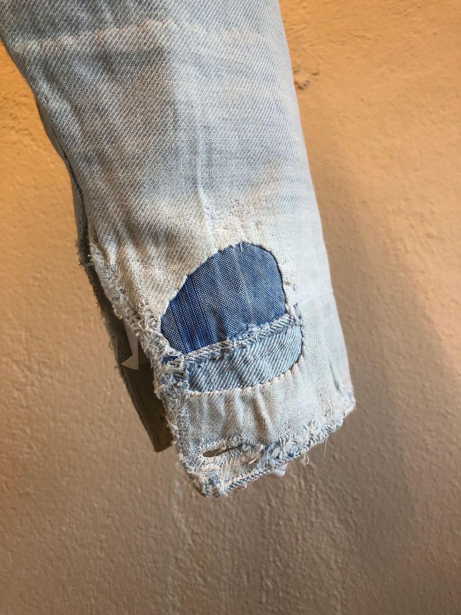 Skjorte til mann. Krageløs linning lukkes med en knapp, åpningen i front lukkes med en knapp. Lange ermer, mansjetter med en knapp. Skjorta er veldig utslitt. Lappet og forsterket på svært mange steder.