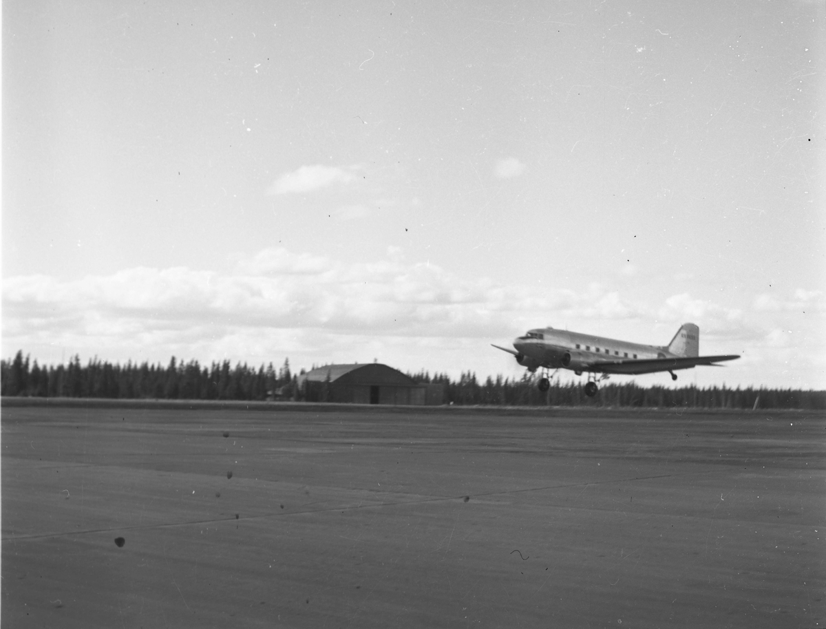 Et passasjerfly ved navn Douglas DC-3 Dakota tar av fra Fornebu flyplass. En hangar sees i bakgrunnen.