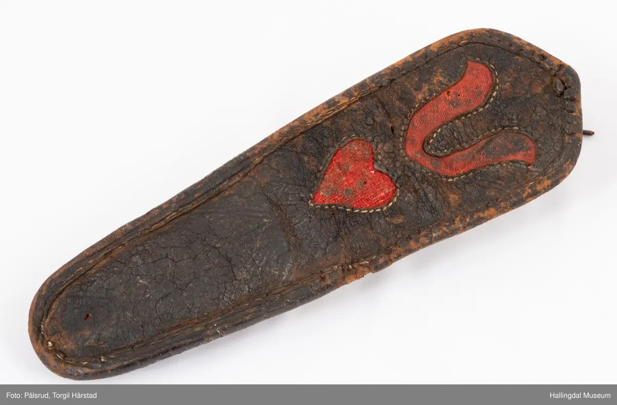 Kniv med etui. 
Etuiet er laget av mørkebrunt lær og ullstoff i grønt, rødt, gult og blått. Den er en tilnærmet rektangulær form som er avrundet i bunn og lokk. Er sydd sammen av to stykker med en ytterside og en innerside. Yttersiden er av mørkebrunt lær med påsydd lærkant. Den bredeste delen kan brettes over som lokk og har en utskjært hjerte- og en utskjært tulipanform. Lokket har på innsiden en lærreim som feste. Begge formene er kantet med lyse sting og foret med rødt ullstoff. 
På innsiden er etuiet foret med grønt ullstoff der de lyse stingene fra formene på lokket er synlig. kniven oppbevares i en av fire lommer som er kantet med grønt, gult, rødt og blått ullstoff. Selve yttersiden av etuiet/eller knivsliren er av mørkebrunt lær, kantet med samme lærkant som yttersiden og lokk, og er dekorert med linjer på sidene. Den er også dekorert med en påsydd lærlomme som er foret med rødt ullstoff som synes på kantene. Sydd med lyse sting og er preget med med et kryss og en V. 

Kniven har et skaft med et utskåret dyrehode (hvalross) og et laget av en hvalrosstann. Noe skadd. Knivbladet er festet gjennom hele lengden av skaftet, er rustent og har avbrekte deler på knivbladet. Knivblad stemplet med P. C./eller O. Westlander.