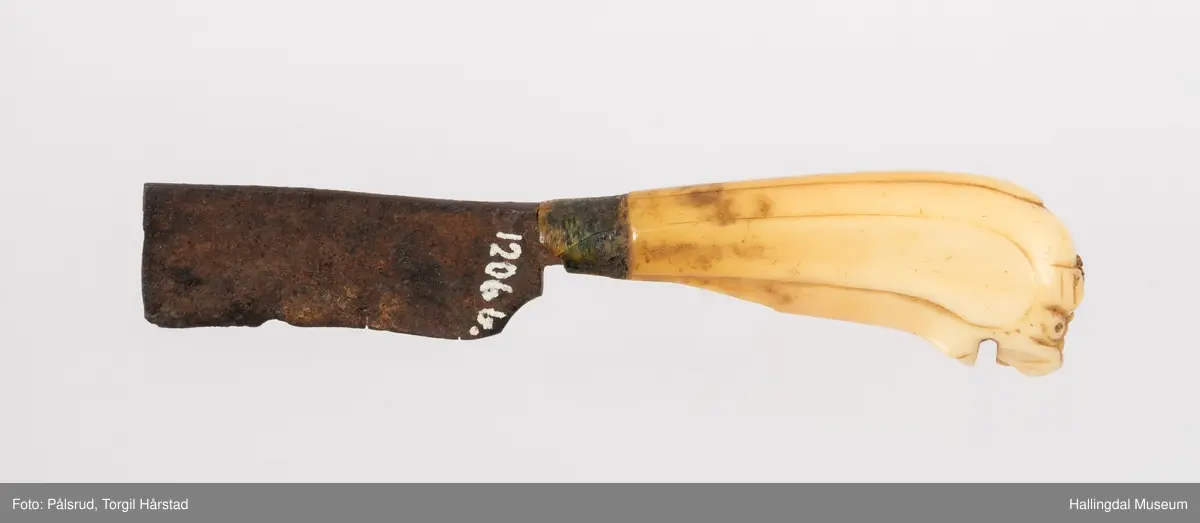 Kniv med etui. 
Etuiet er laget av mørkebrunt lær og ullstoff i grønt, rødt, gult og blått. Den er en tilnærmet rektangulær form som er avrundet i bunn og lokk. Er sydd sammen av to stykker med en ytterside og en innerside. Yttersiden er av mørkebrunt lær med påsydd lærkant. Den bredeste delen kan brettes over som lokk og har en utskjært hjerte- og en utskjært tulipanform. Lokket har på innsiden en lærreim som feste. Begge formene er kantet med lyse sting og foret med rødt ullstoff. 
På innsiden er etuiet foret med grønt ullstoff der de lyse stingene fra formene på lokket er synlig. kniven oppbevares i en av fire lommer som er kantet med grønt, gult, rødt og blått ullstoff. Selve yttersiden av etuiet/eller knivsliren er av mørkebrunt lær, kantet med samme lærkant som yttersiden og lokk, og er dekorert med linjer på sidene. Den er også dekorert med en påsydd lærlomme som er foret med rødt ullstoff som synes på kantene. Sydd med lyse sting og er preget med med et kryss og en V. 

Kniven har et skaft med et utskåret dyrehode (hvalross) og et laget av en hvalrosstann. Noe skadd. Knivbladet er festet gjennom hele lengden av skaftet, er rustent og har avbrekte deler på knivbladet. Knivblad stemplet med P. C./eller O. Westlander.