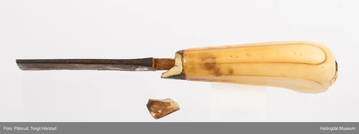 Kniv med etui. 
Etuiet er laget av mørkebrunt lær og ullstoff i grønt, rødt, gult og blått. Den er en tilnærmet rektangulær form som er avrundet i bunn og lokk. Er sydd sammen av to stykker med en ytterside og en innerside. Yttersiden er av mørkebrunt lær med påsydd lærkant. Den bredeste delen kan brettes over som lokk og har en utskjært hjerte- og en utskjært tulipanform. Lokket har på innsiden en lærreim som feste. Begge formene er kantet med lyse sting og foret med rødt ullstoff. 
På innsiden er etuiet foret med grønt ullstoff der de lyse stingene fra formene på lokket er synlig. kniven oppbevares i en av fire lommer som er kantet med grønt, gult, rødt og blått ullstoff. Selve yttersiden av etuiet/eller knivsliren er av mørkebrunt lær, kantet med samme lærkant som yttersiden og lokk, og er dekorert med linjer på sidene. Den er også dekorert med en påsydd lærlomme som er foret med rødt ullstoff som synes på kantene. Sydd med lyse sting og er preget med med et kryss og en V. 

Kniven har et skaft med et utskåret dyrehode (hvalross) og et laget av en hvalrosstann. Noe skadd. Knivbladet er festet gjennom hele lengden av skaftet, er rustent og har avbrekte deler på knivbladet. Knivblad stemplet med P. C./eller O. Westlander.