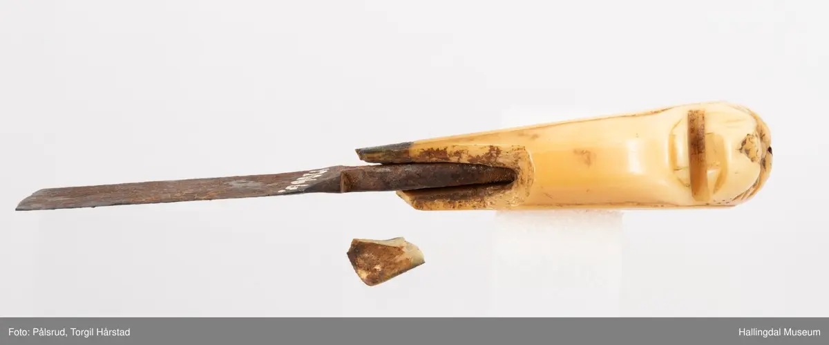 Kniv med etui. 
Etuiet er laget av mørkebrunt lær og ullstoff i grønt, rødt, gult og blått. Den er en tilnærmet rektangulær form som er avrundet i bunn og lokk. Er sydd sammen av to stykker med en ytterside og en innerside. Yttersiden er av mørkebrunt lær med påsydd lærkant. Den bredeste delen kan brettes over som lokk og har en utskjært hjerte- og en utskjært tulipanform. Lokket har på innsiden en lærreim som feste. Begge formene er kantet med lyse sting og foret med rødt ullstoff. 
På innsiden er etuiet foret med grønt ullstoff der de lyse stingene fra formene på lokket er synlig. kniven oppbevares i en av fire lommer som er kantet med grønt, gult, rødt og blått ullstoff. Selve yttersiden av etuiet/eller knivsliren er av mørkebrunt lær, kantet med samme lærkant som yttersiden og lokk, og er dekorert med linjer på sidene. Den er også dekorert med en påsydd lærlomme som er foret med rødt ullstoff som synes på kantene. Sydd med lyse sting og er preget med med et kryss og en V. 

Kniven har et skaft med et utskåret dyrehode (hvalross) og et laget av en hvalrosstann. Noe skadd. Knivbladet er festet gjennom hele lengden av skaftet, er rustent og har avbrekte deler på knivbladet. Knivblad stemplet med P. C./eller O. Westlander.