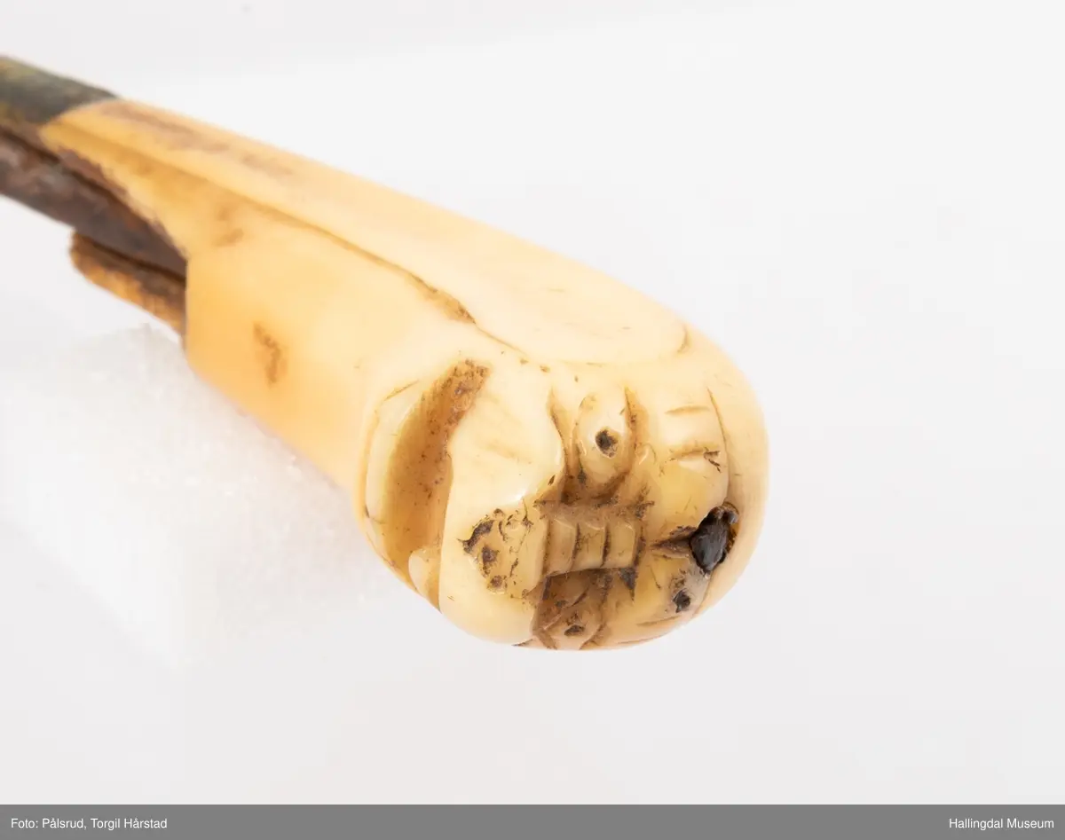 Kniv med etui. 
Etuiet er laget av mørkebrunt lær og ullstoff i grønt, rødt, gult og blått. Den er en tilnærmet rektangulær form som er avrundet i bunn og lokk. Er sydd sammen av to stykker med en ytterside og en innerside. Yttersiden er av mørkebrunt lær med påsydd lærkant. Den bredeste delen kan brettes over som lokk og har en utskjært hjerte- og en utskjært tulipanform. Lokket har på innsiden en lærreim som feste. Begge formene er kantet med lyse sting og foret med rødt ullstoff. 
På innsiden er etuiet foret med grønt ullstoff der de lyse stingene fra formene på lokket er synlig. kniven oppbevares i en av fire lommer som er kantet med grønt, gult, rødt og blått ullstoff. Selve yttersiden av etuiet/eller knivsliren er av mørkebrunt lær, kantet med samme lærkant som yttersiden og lokk, og er dekorert med linjer på sidene. Den er også dekorert med en påsydd lærlomme som er foret med rødt ullstoff som synes på kantene. Sydd med lyse sting og er preget med med et kryss og en V. 

Kniven har et skaft med et utskåret dyrehode (hvalross) og et laget av en hvalrosstann. Noe skadd. Knivbladet er festet gjennom hele lengden av skaftet, er rustent og har avbrekte deler på knivbladet. Knivblad stemplet med P. C./eller O. Westlander.