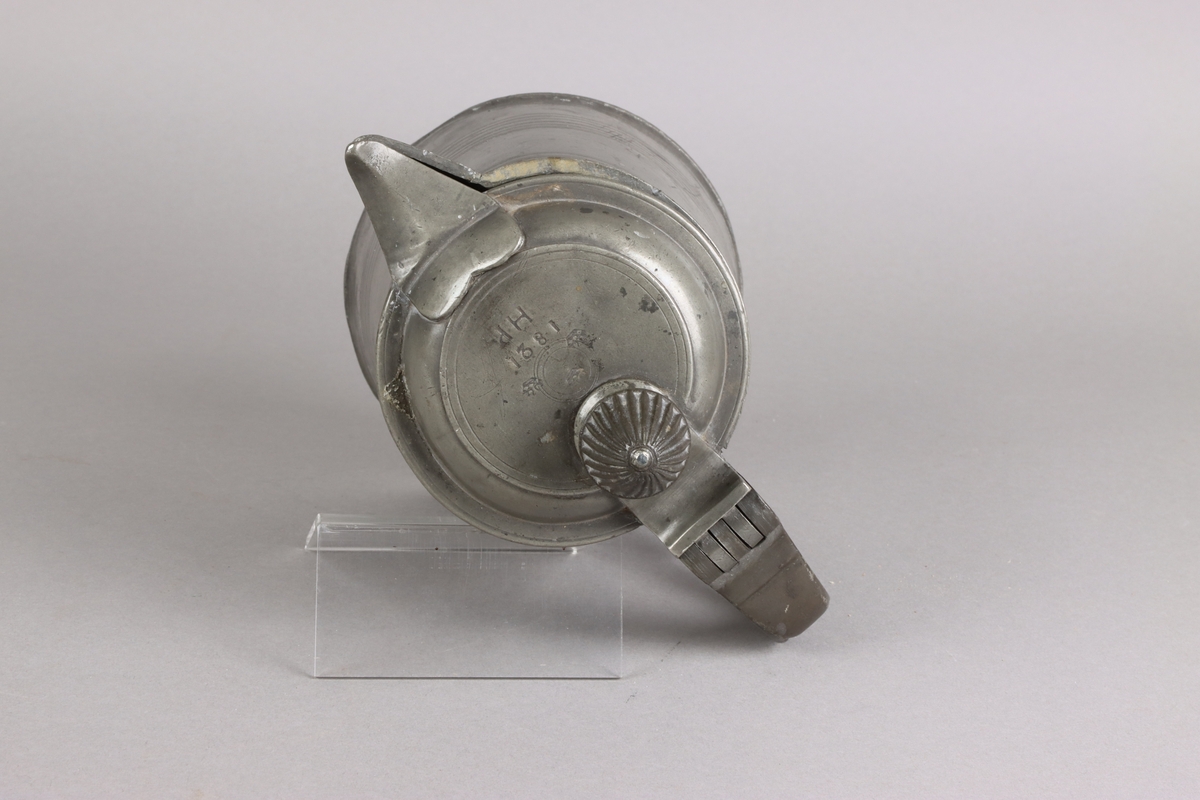 Jug and cover, all in pewter, with conical body  and a loop handle. On the cover knob in the form of a pine cone. On the body sections of horizontal borders. Five hallmarks inside the jug.