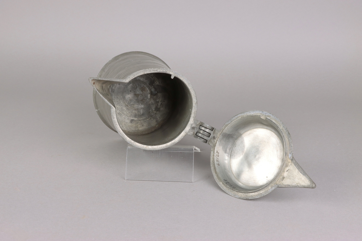 Jug and cover, all in pewter, with conical body  and a loop handle. On the cover knob in the form of a pine cone. On the body sections of horizontal borders. Five hallmarks inside the jug.
