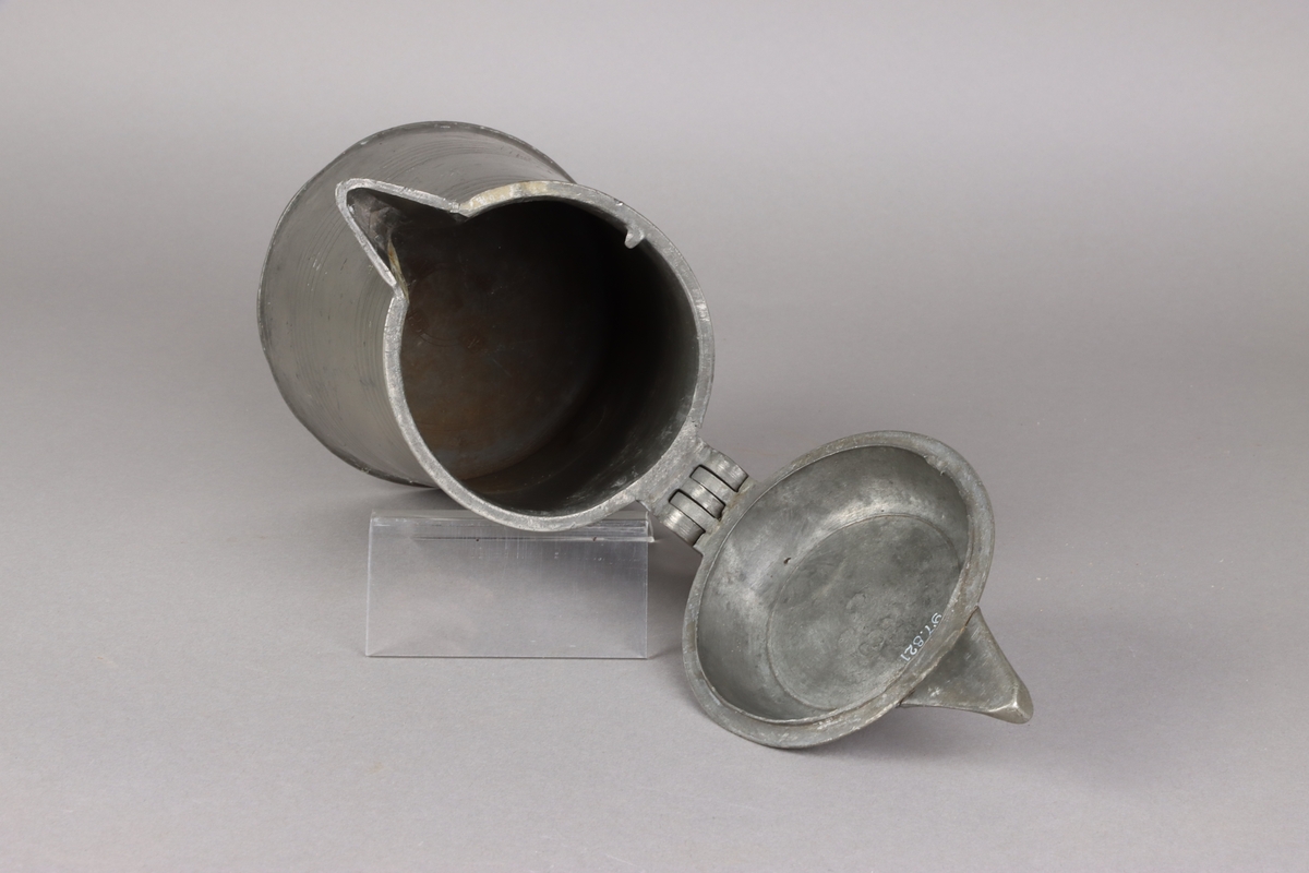 Jug and cover, all in pewter, with conical body  and a loop handle. On the cover knob in the form of a pine cone. On the body sections of horizontal borders. Five hallmarks inside the jug.