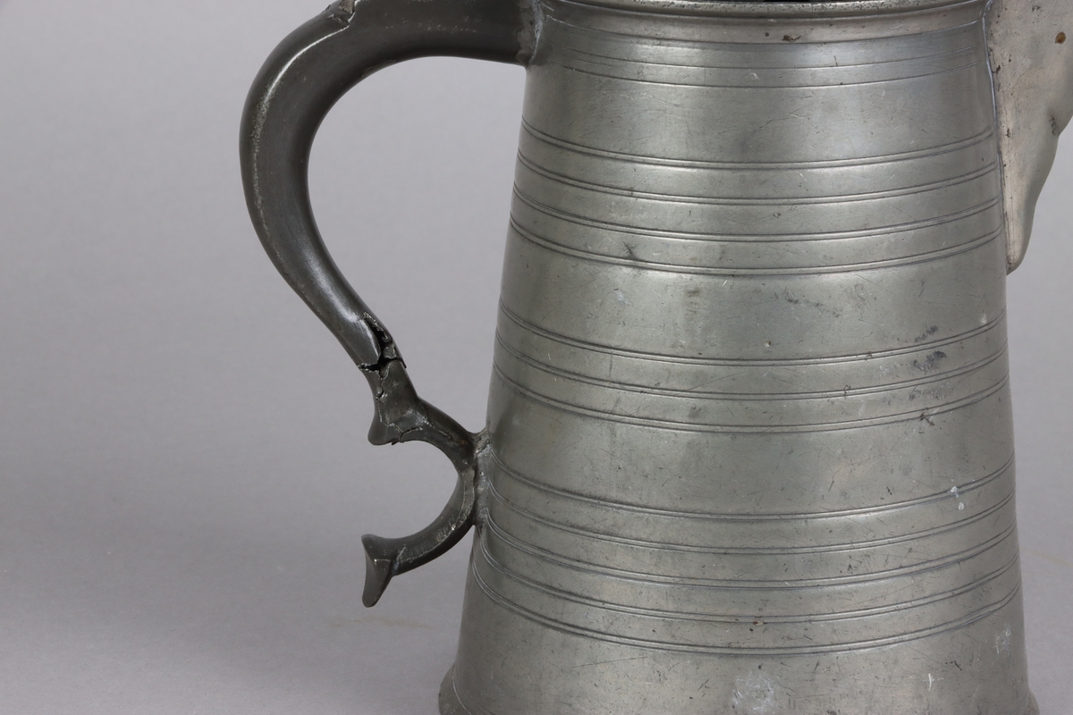 Jug and cover, all in pewter, with conical body  and a loop handle. On the cover knob in the form of a pine cone. On the body sections of horizontal borders. Five hallmarks inside the jug.

