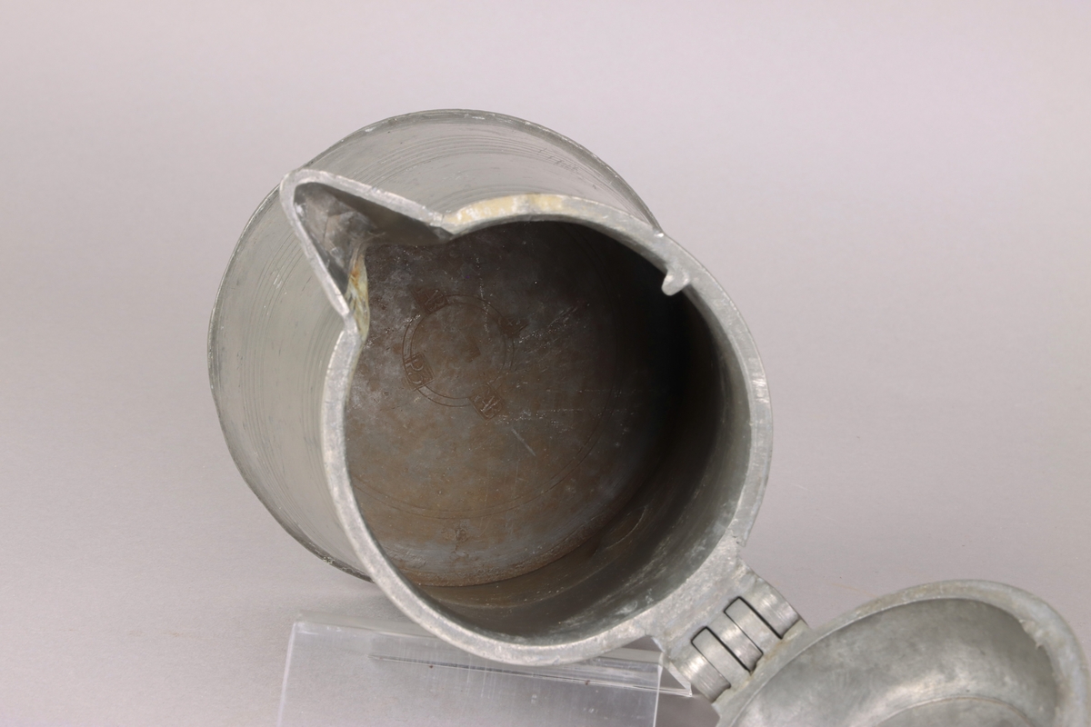 Jug and cover, all in pewter, with conical body  and a loop handle. On the cover knob in the form of a pine cone. On the body sections of horizontal borders. Five hallmarks inside the jug.