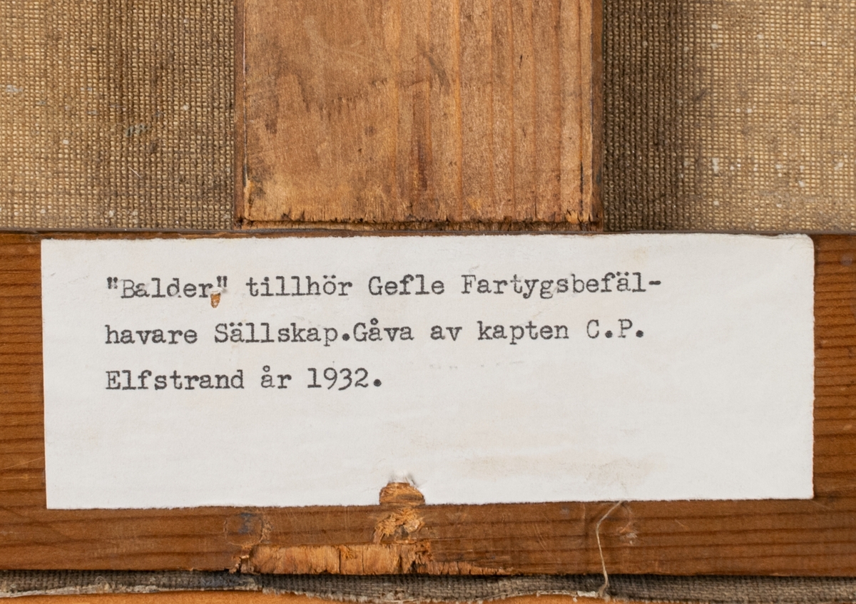 Tavla med ram. Olja på duk. Motiv: Ångfartyget "Balder" till havs. Seglar från höger till vänster. Tvåmastad med röd-grå-svart skrov och vitsvart skorsten. I akter svensk unionsflagga med norskt unionsmärke. Den molniga himlen och vattnet har turkosgrön färgton (ev. sekundär effekt). I bakgrunden segelfartyg och till höger skymtar land. Ångfartyget byggdes 1872 för P.J. Haegerstrand rederi i Gävle och såldes 1909 till Dunkerque. Signatur nere till vänster: Ralph Lagye" (osäker). Etiketter på baksidan  med förvärvshistorik och lista över befälhavare med årtal. Profilerad, förgylld träram utan ornamentik. Duk spänd på kilram.