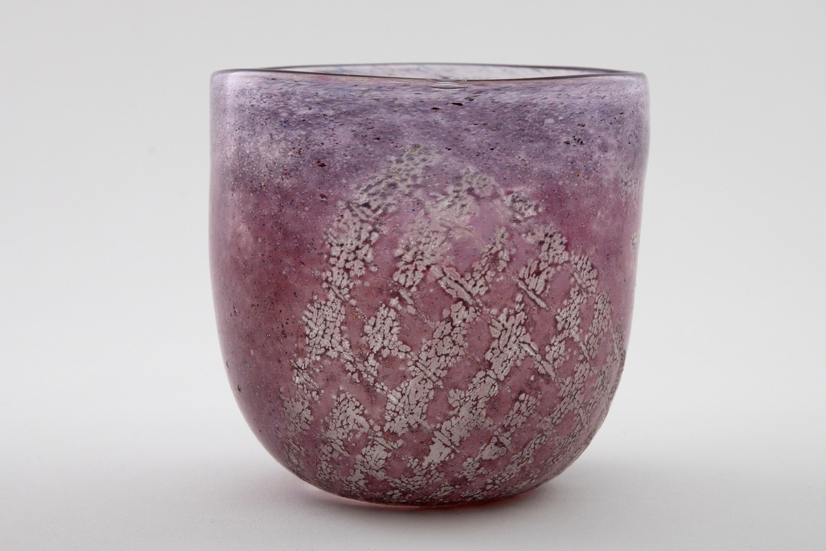 Tilnærmet sylindrisk bolle i halvgjennomskinnelig glass. Overflaten er dekorert med lilla og rødlig emaljefarge samt glassfiber, som danner et rutemønster på bollens nedre del.