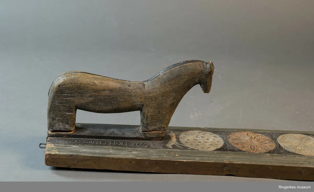 Laget av massivt tre med innfelt hest. Krok av jern i enden, antageligvis sekundær. Rester av lær festet med 3 spiker i enden, antagelig gammelt oppheng. Håndtaket er formet som en hest med man, hvite øyne, ører, og mule. Panneluggen er pent utskåret. Ett øre er ødelagt. Hesten har hale. Man og hale er malt svarte, og det går en svart strek langs ryggen til hesten fra man til hale. Denne er også svart. Halen er kort. Det er en sprekk mellom hesten og mangletreet. Rundt hesten er det innrisset skrift, og to små rosetter i karveskurd, diameter 1.5 cm. Relieff av hund foran hestens forbein. Hunden er malt i grågrønn farge. 

Det er 7 rosetter skåret ut på mangletreet. Hver rosett har sitt spesifikke mønster. Rosett 1,2,3,5,6 har blomstermønster. 4 og 7 har virvler. Annenhver rosett er malt med grågrønn, og annenhver med brun farge. Feltet rundt rosettene er malt svart, med noe utydelig dekor, og tallene 1808 mellom hver rosett fra 3. til 7. På motsatt side er bokstavene JSSS skåret inn. Mangletreet har et grønt felt utenfor det svarte, dette er skåret til en pen profil. Mangletreet bærer i det hele tatt preg av høy kvalitet på håndverket.