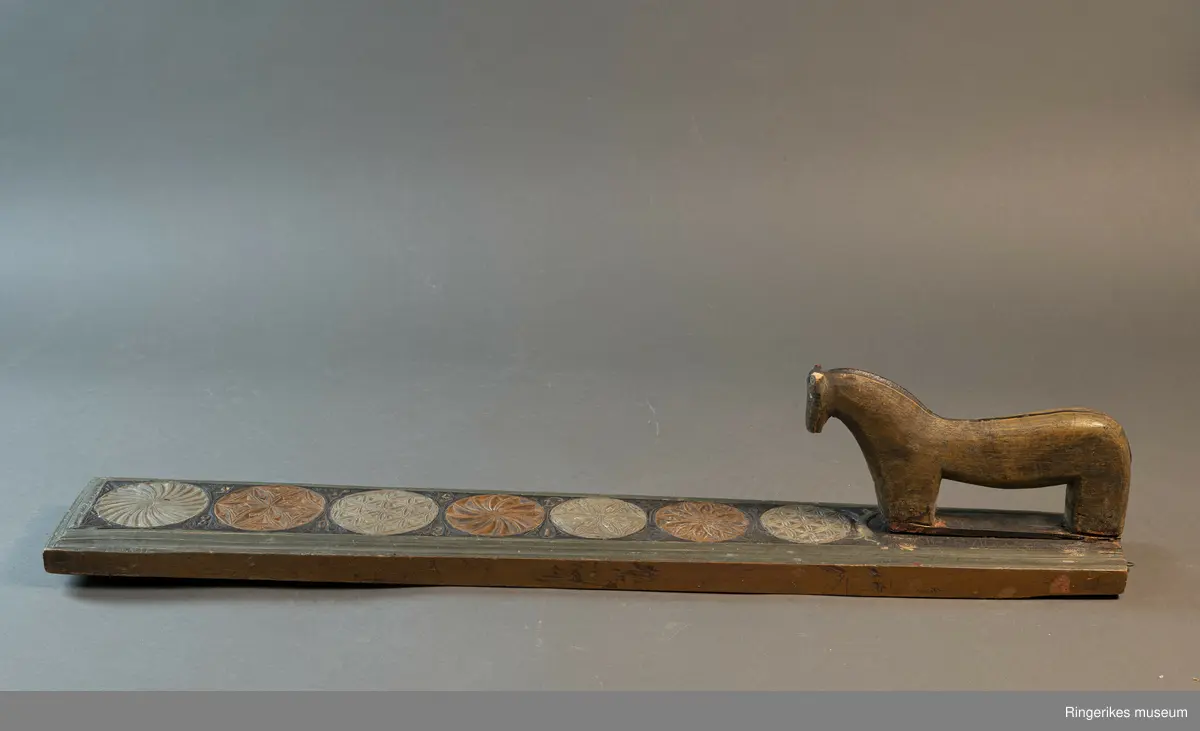 Laget av massivt tre med innfelt hest. Krok av jern i enden, antageligvis sekundær. Rester av lær festet med 3 spiker i enden, antagelig gammelt oppheng. Håndtaket er formet som en hest med man, hvite øyne, ører, og mule. Panneluggen er pent utskåret. Ett øre er ødelagt. Hesten har hale. Man og hale er malt svarte, og det går en svart strek langs ryggen til hesten fra man til hale. Denne er også svart. Halen er kort. Det er en sprekk mellom hesten og mangletreet. Rundt hesten er det innrisset skrift, og to små rosetter i karveskurd, diameter 1.5 cm. Relieff av hund foran hestens forbein. Hunden er malt i grågrønn farge. 

Det er 7 rosetter skåret ut på mangletreet. Hver rosett har sitt spesifikke mønster. Rosett 1,2,3,5,6 har blomstermønster. 4 og 7 har virvler. Annenhver rosett er malt med grågrønn, og annenhver med brun farge. Feltet rundt rosettene er malt svart, med noe utydelig dekor, og tallene 1808 mellom hver rosett fra 3. til 7. På motsatt side er bokstavene JSSS skåret inn. Mangletreet har et grønt felt utenfor det svarte, dette er skåret til en pen profil. Mangletreet bærer i det hele tatt preg av høy kvalitet på håndverket.