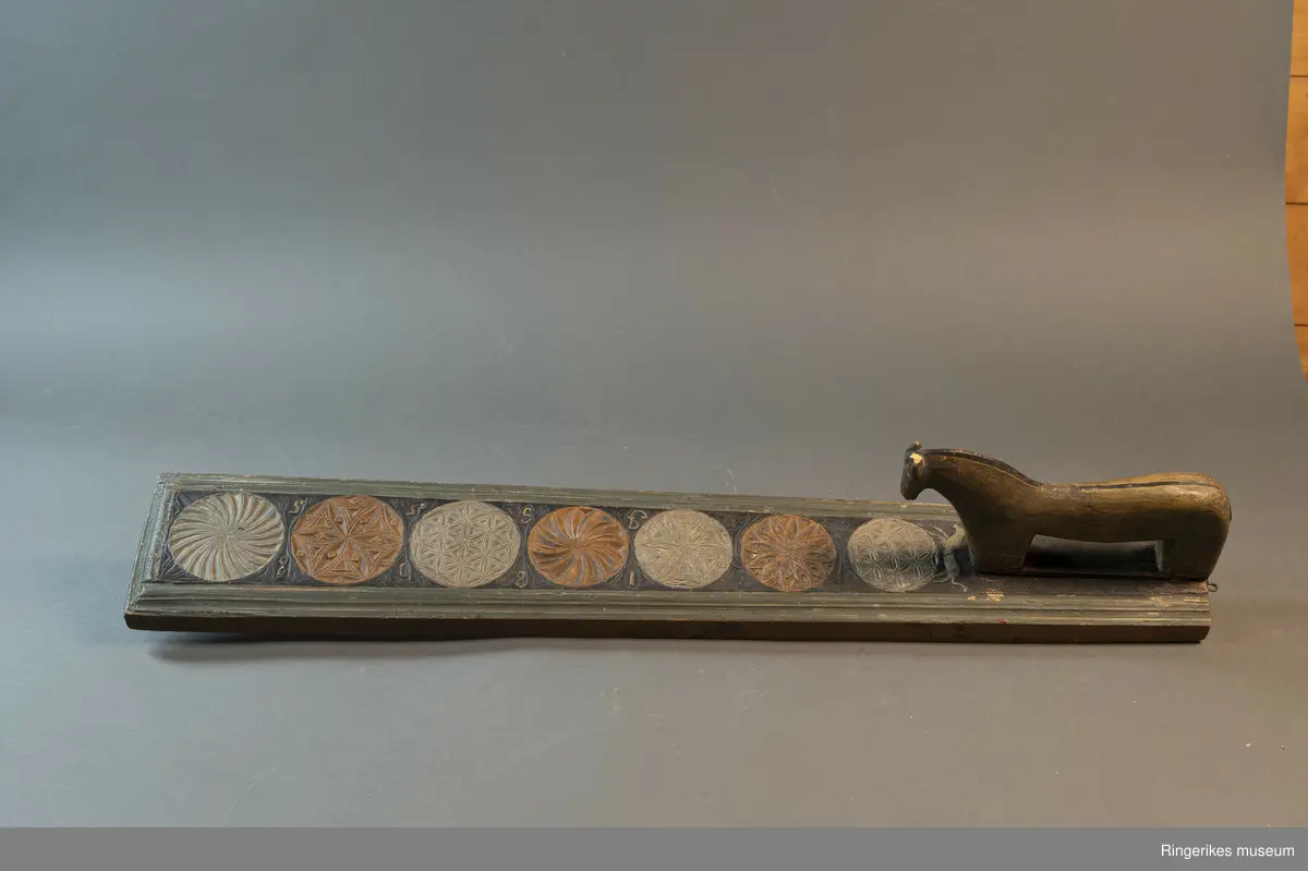 Laget av massivt tre med innfelt hest. Krok av jern i enden, antageligvis sekundær. Rester av lær festet med 3 spiker i enden, antagelig gammelt oppheng. Håndtaket er formet som en hest med man, hvite øyne, ører, og mule. Panneluggen er pent utskåret. Ett øre er ødelagt. Hesten har hale. Man og hale er malt svarte, og det går en svart strek langs ryggen til hesten fra man til hale. Denne er også svart. Halen er kort. Det er en sprekk mellom hesten og mangletreet. Rundt hesten er det innrisset skrift, og to små rosetter i karveskurd, diameter 1.5 cm. Relieff av hund foran hestens forbein. Hunden er malt i grågrønn farge. 

Det er 7 rosetter skåret ut på mangletreet. Hver rosett har sitt spesifikke mønster. Rosett 1,2,3,5,6 har blomstermønster. 4 og 7 har virvler. Annenhver rosett er malt med grågrønn, og annenhver med brun farge. Feltet rundt rosettene er malt svart, med noe utydelig dekor, og tallene 1808 mellom hver rosett fra 3. til 7. På motsatt side er bokstavene JSSS skåret inn. Mangletreet har et grønt felt utenfor det svarte, dette er skåret til en pen profil. Mangletreet bærer i det hele tatt preg av høy kvalitet på håndverket.