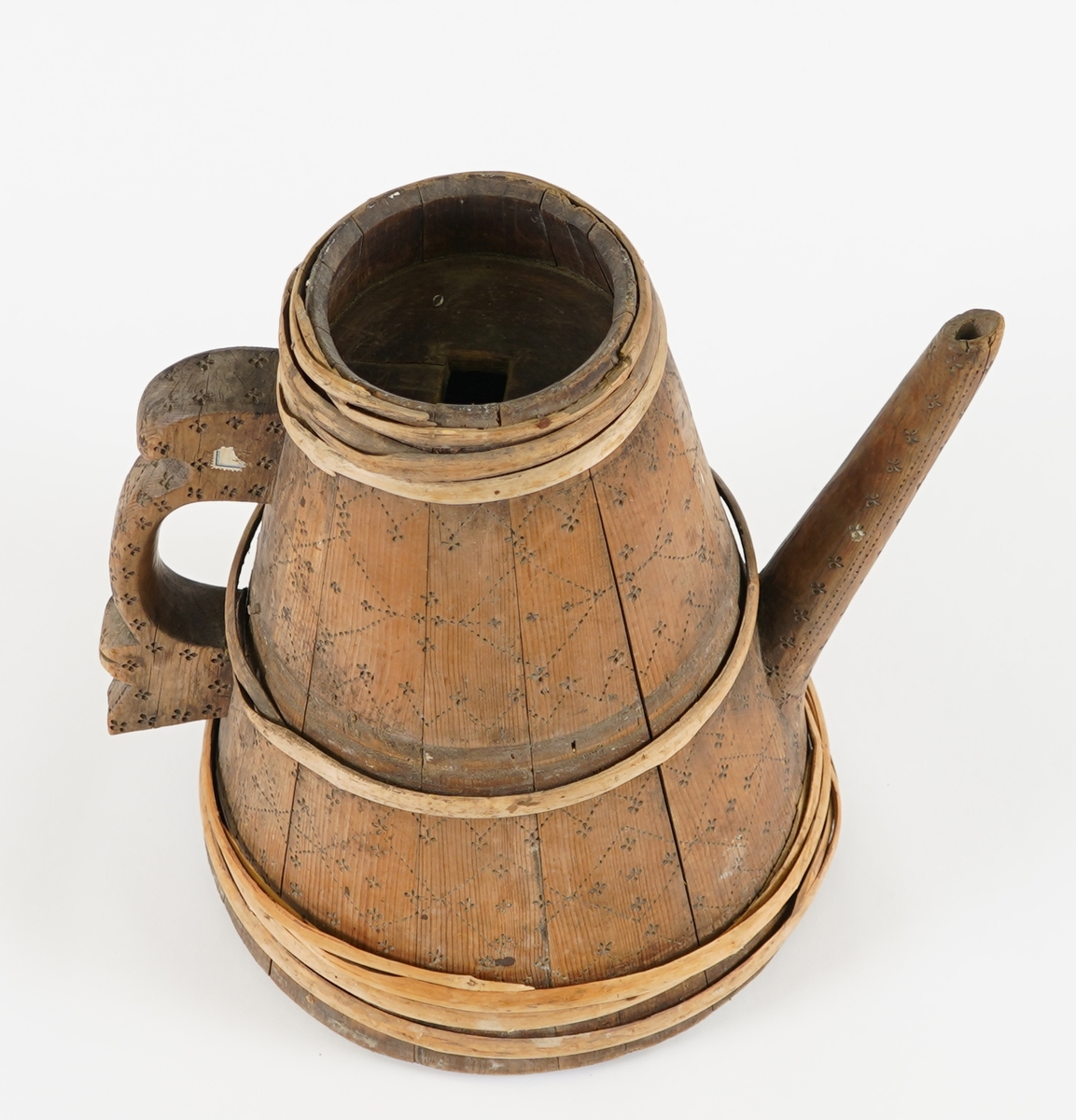 Ei lagga kanne, med konisk form. Sett saman av tretten stavar og sju vidjeband. Den eine staven har ei uthola grein, som fungerer som tut på kanna. Staven på motsett side av denne har skore til ein hank av same stykke. Innfelt fast topp- og botnstykke. Firkanta hol i midten av toppstykket. Svidekor på heile utsida.