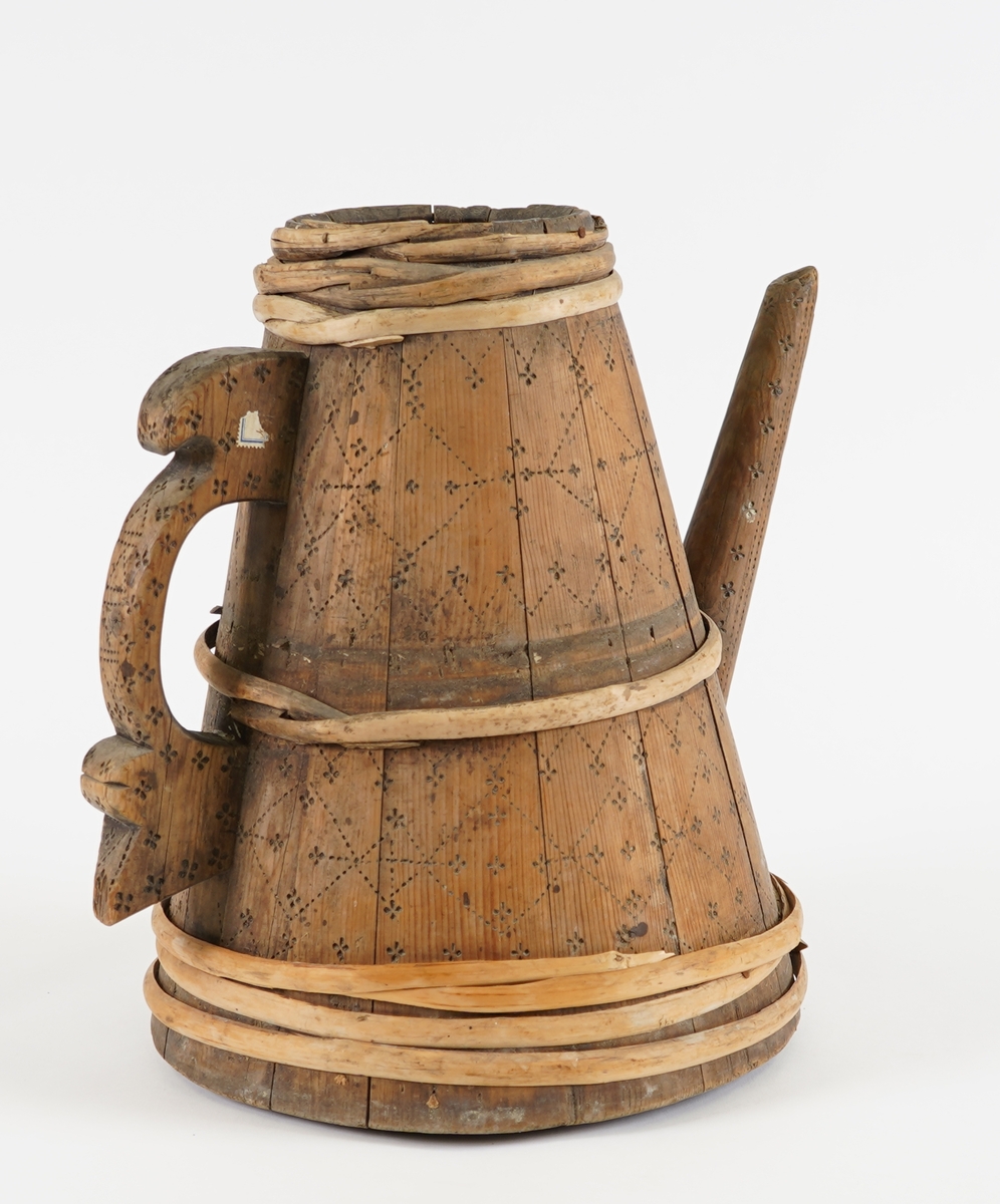 Ei lagga kanne, med konisk form. Sett saman av tretten stavar og sju vidjeband. Den eine staven har ei uthola grein, som fungerer som tut på kanna. Staven på motsett side av denne har skore til ein hank av same stykke. Innfelt fast topp- og botnstykke. Firkanta hol i midten av toppstykket. Svidekor på heile utsida.