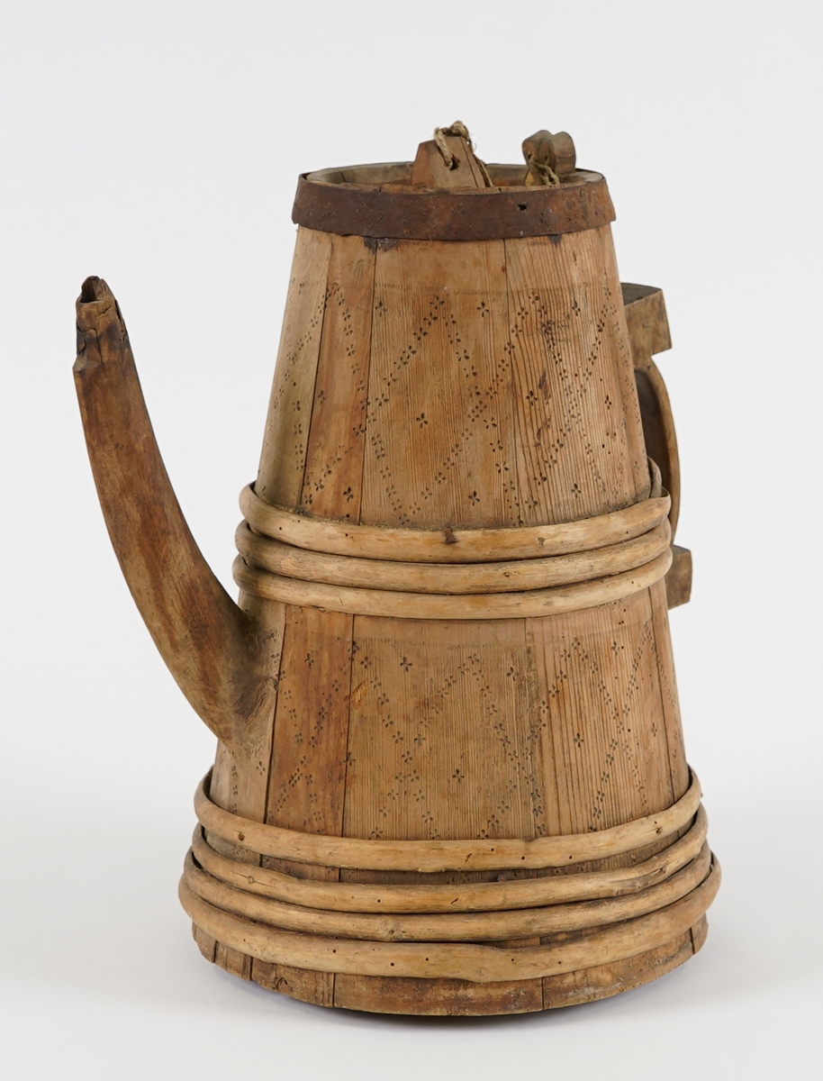 Ei lagga kanne, med konisk form. Sett saman av ti stavar og åtte vidjeband - sju av tre og eitt av jern. Den eine staven har ei uthola grein, som fungerer som tut på kanna. Staven på motsett side av denne har skore til ein hank av same stykke. Innfelt fast toppstykke med hol i midten, tetta med ein tapp som er knytt fast med hyssing i toppen av staven med hank. Svidekor på korpus, og utskjeringar på hanken.