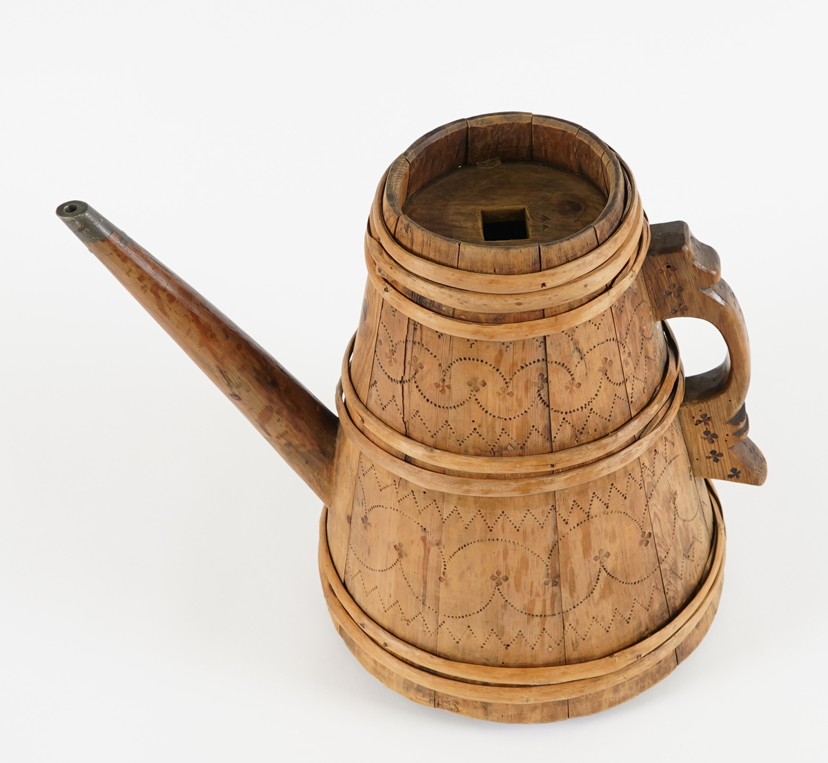 Ei lagga kanne, med konisk form. Sett saman av ti stavar og sju vidjeband. Den eine staven har ei uthola grein, som fungerer som tut på kanna. Staven på motsett side av denne har skore til ein hank av same stykke. Innfelt fast toppstykke med hol i midten. Svidekor på korpus og hanken.