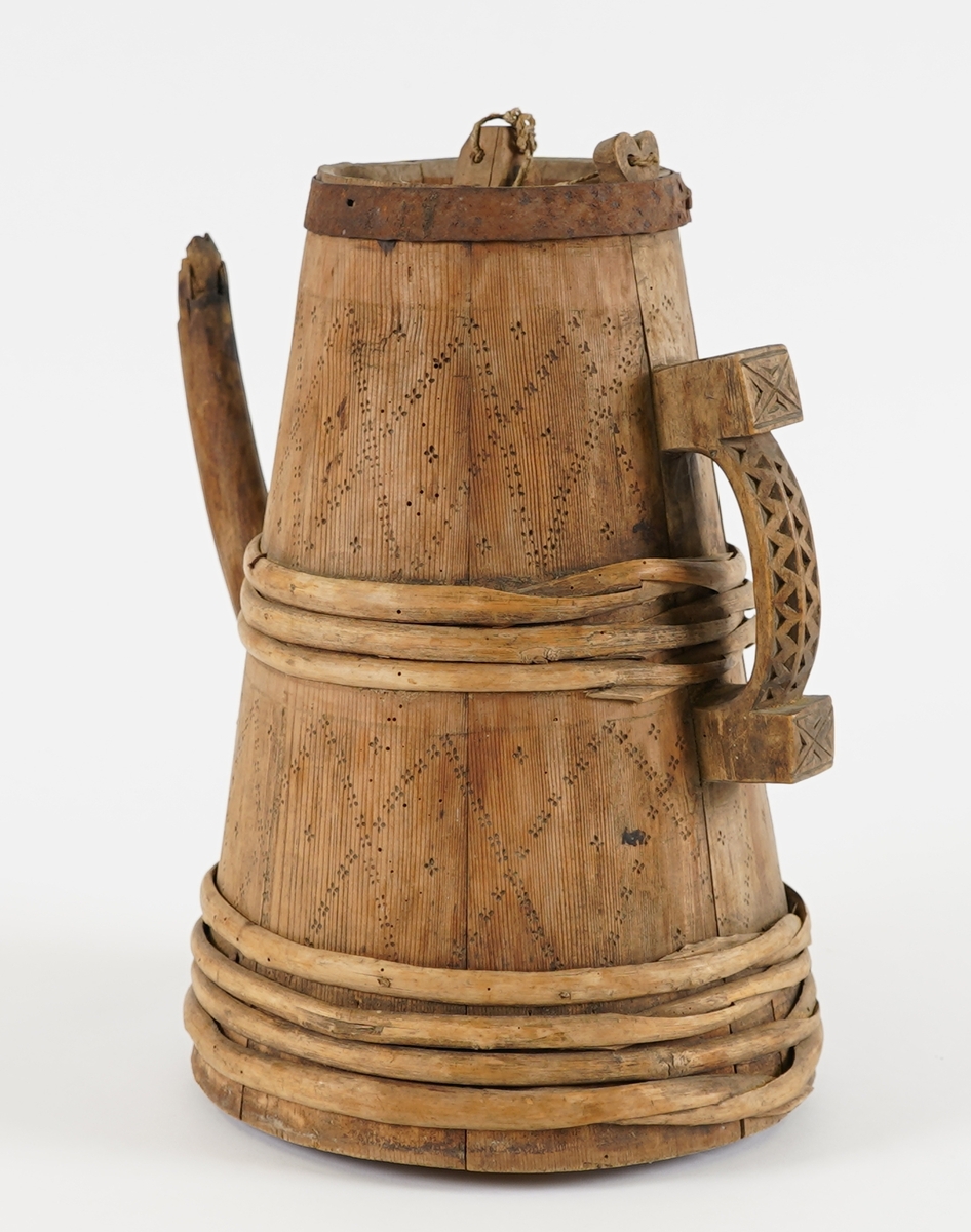 Ei lagga kanne, med konisk form. Sett saman av ti stavar og åtte vidjeband - sju av tre og eitt av jern. Den eine staven har ei uthola grein, som fungerer som tut på kanna. Staven på motsett side av denne har skore til ein hank av same stykke. Innfelt fast toppstykke med hol i midten, tetta med ein tapp som er knytt fast med hyssing i toppen av staven med hank. Svidekor på korpus, og utskjeringar på hanken.