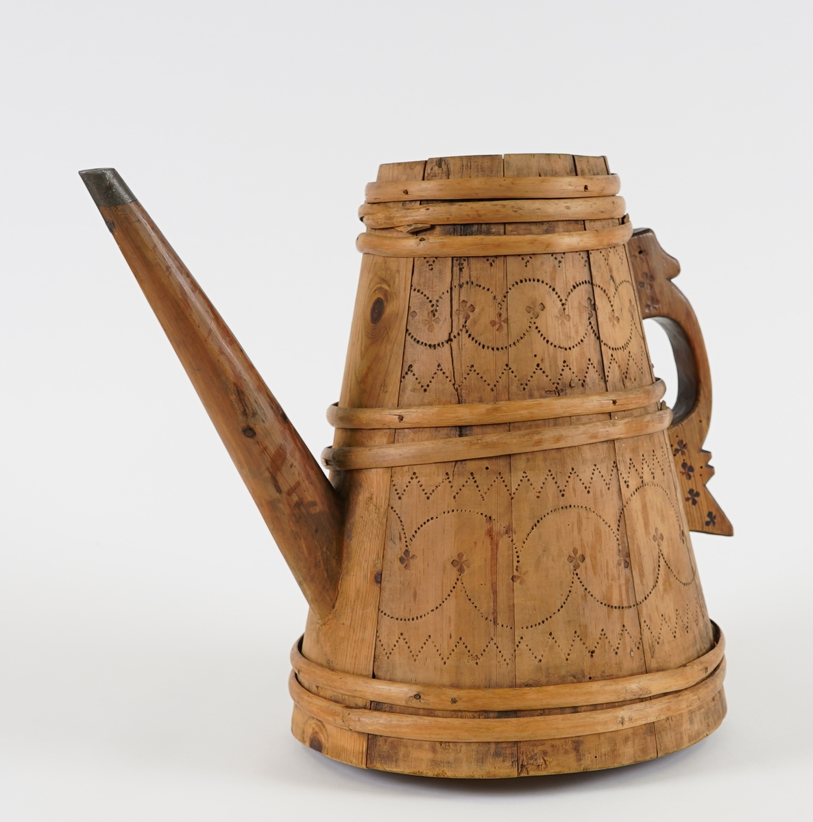 Ei lagga kanne, med konisk form. Sett saman av ti stavar og sju vidjeband. Den eine staven har ei uthola grein, som fungerer som tut på kanna. Staven på motsett side av denne har skore til ein hank av same stykke. Innfelt fast toppstykke med hol i midten. Svidekor på korpus og hanken.