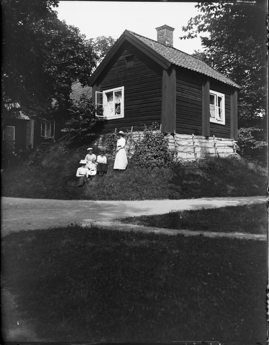 Kvinnor sitter i gräset vid en stuga, Sätra brunn, Sala