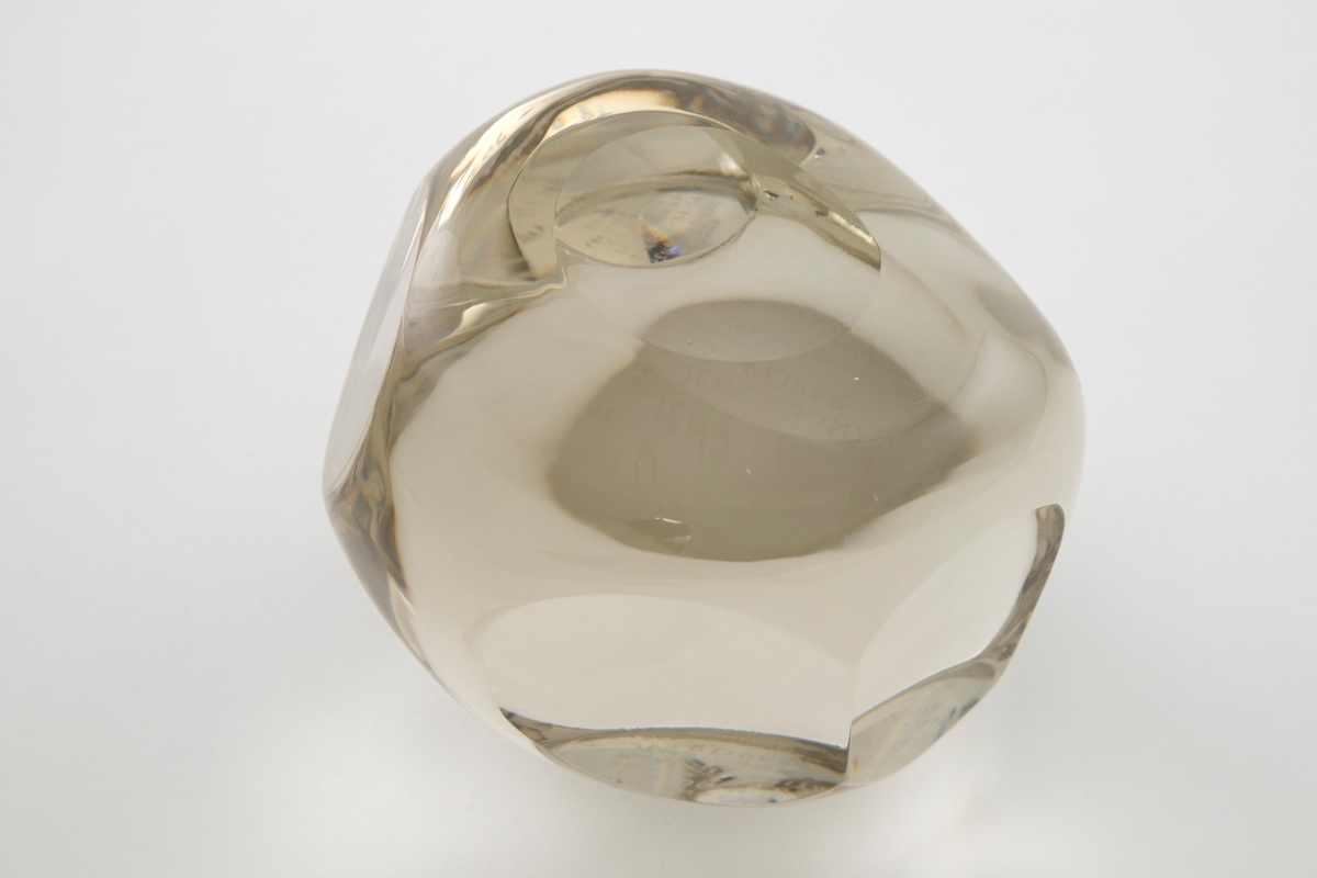 Irregulær kuleformet skulptur av massiv klart glass med slipte ovalformede og runde partier på yttersiden.