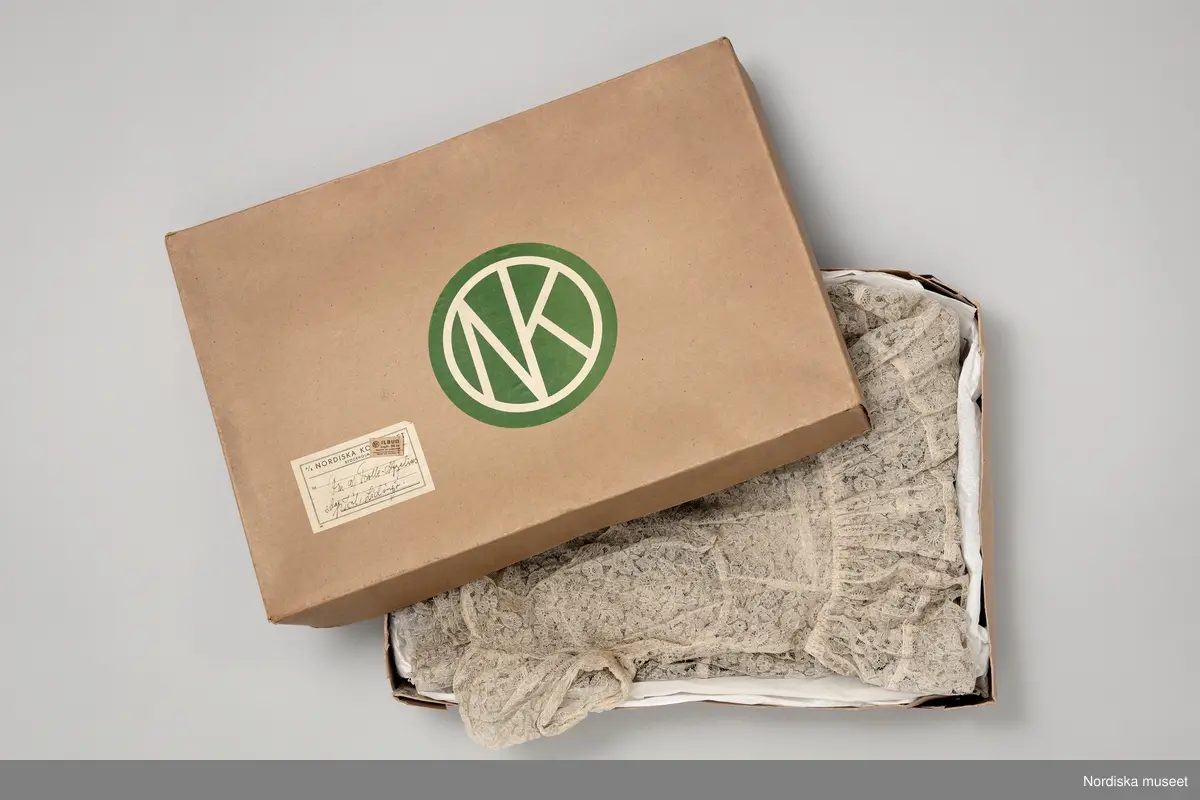 Paket från NK:s Franska damskrädderi.
När det handsydda plagget var avsynat och klart packades det ner med silkespapper i en NK-kartong innan budet tog vid. Stamkunden Elsa af Trolles klänning levererades med ilbud.