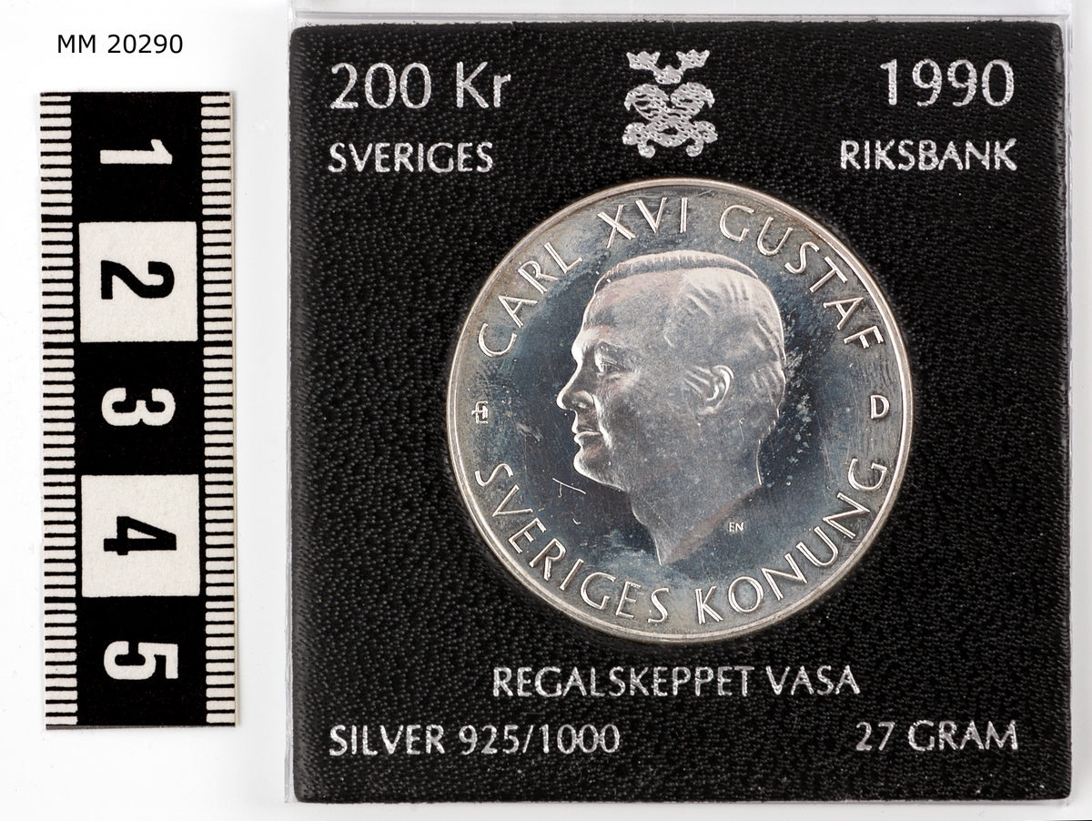 Minnesmynt av silver. Åtsida: Konungens huvud i profil, runt kanten text: "Carl XVI Gustaf, Sveriges Konung". Frånsida: Bild på Vasa samt text: "Regalskeppet Vasa, 15 Juni, 1990, 200 kronor".

Myntet är infattat i fodral av genomskinlig plast, med svart pappers ram runt omkring själva myntet. Text på ramen: Minnesmynt, Regalskeppet Vasa, för invigningen av det nya Vasamuseét, 15 Juni, 1990. FAKTA: Valör: 200 Skr, Metall: Silver, Vikt: 27,03 g, Diameter: 36mm, Upplaga: 50000, Konstnär: Ernst Nordin, Tillverkare: AB Tumba Bruk, Myntverket, Eskilstuna, Utgivare: Sveriges Riksbank.

Informationshäfte se inventariebilaga.