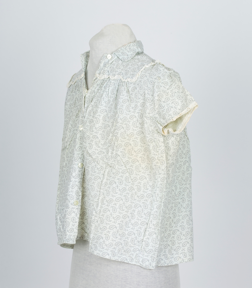 Pyjamas, fllanellignende stogg påtrykt dråpemønster med blomst inni. 

A: Overdel 
Forknappet, 5 knapper og knapphull. Krage. Firkantet bærestykke kantet med maskinlaget engelsk blonde. Kort erme kantet med engelsk blonde.
B: Bukse
Knebukse. Løpegang for strikk i livet. Engelsk blondekant på bukseben.