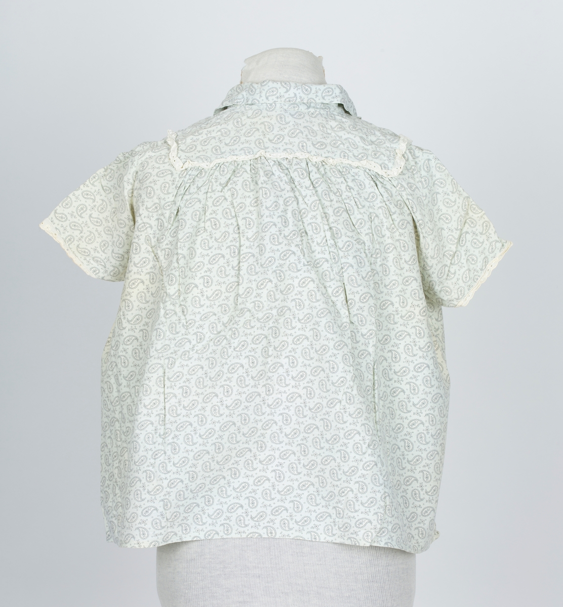 Pyjamas, fllanellignende stogg påtrykt dråpemønster med blomst inni. 

A: Overdel 
Forknappet, 5 knapper og knapphull. Krage. Firkantet bærestykke kantet med maskinlaget engelsk blonde. Kort erme kantet med engelsk blonde.
B: Bukse
Knebukse. Løpegang for strikk i livet. Engelsk blondekant på bukseben.