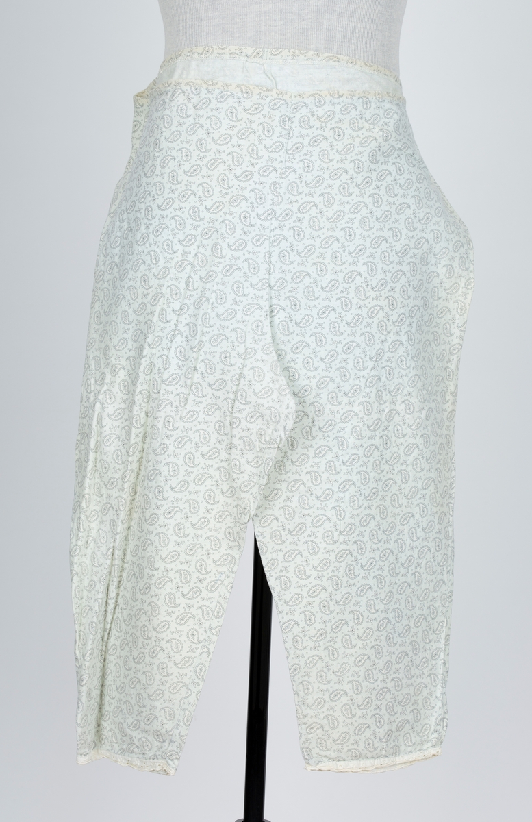 Pyjamas, fllanellignende stogg påtrykt dråpemønster med blomst inni. 

A: Overdel 
Forknappet, 5 knapper og knapphull. Krage. Firkantet bærestykke kantet med maskinlaget engelsk blonde. Kort erme kantet med engelsk blonde.
B: Bukse
Knebukse. Løpegang for strikk i livet. Engelsk blondekant på bukseben.