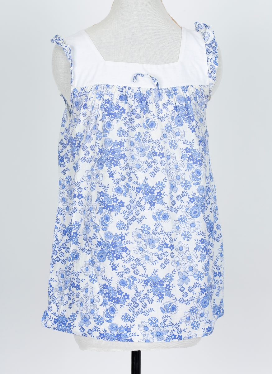 Baby doll. 2-delt nattøy. Stoff i tynn polyester/bomullsblanding, hvit bunn med blå blomstertrykk
A: Overdel
Firkantet hvitt bærestykke og halsåpning. Sommerfugl rysj over skulder. "skjørt" lett rynket til bærestykket. Smal sløyfe av stoffet midt på bærestykket.
B: Truse
Hvit, Blå strikkanter i livet og rundt benåpning.