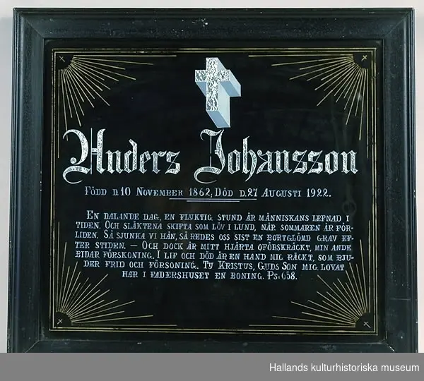 Begravningstavla målad på glas. a) Svart bakgrund. Den dödes namn samt ett kors ovanför i stanniolpapper, (fästat på baksidan). I varje hörn en sol som strålar mot centrum. b) Ram, bredd 3,5 cm. Ram av trä, profilerad. Svartmålad.Text: "Anders Johansson Född d. 10 November 1862"