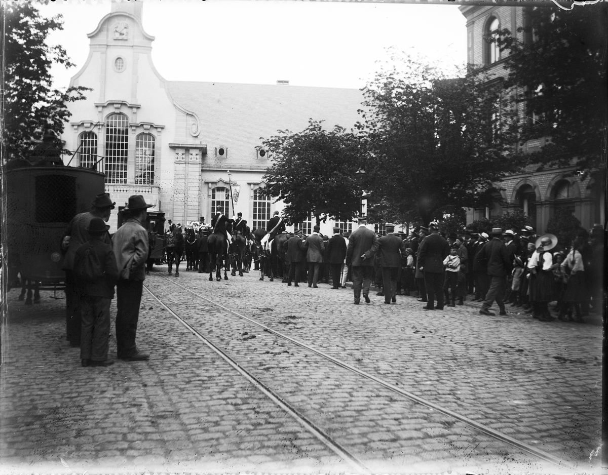 Folksamling och ryttare i uniform i stadsmiljö