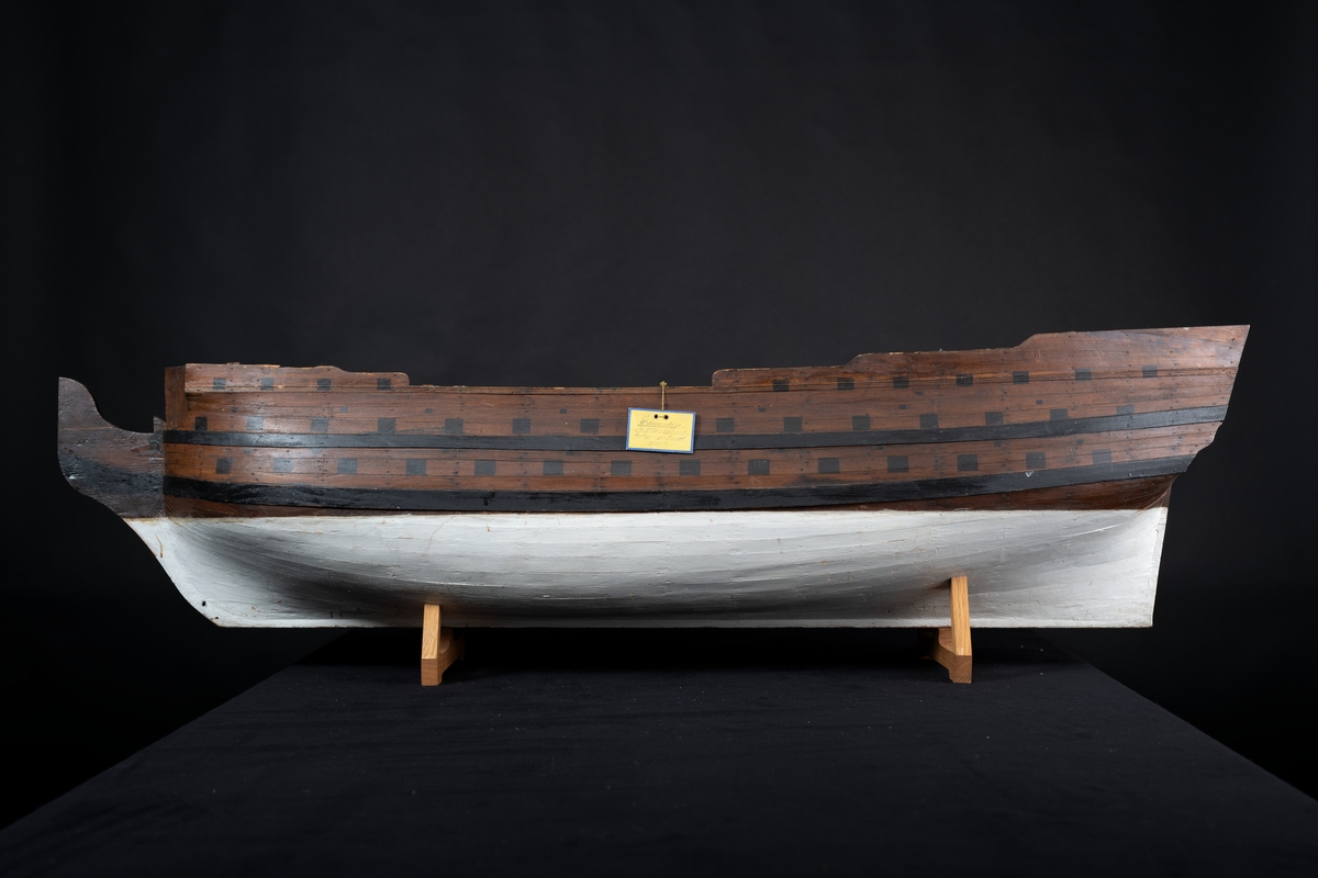 Fartygsmodell 80-kanonskepp efter 1765 års reglemente. Skrovmodell. Bordläggningen limmad på gavlar, utan inredning, galjon och akterspegel. Modellen brunmålad med svarta kanonportar och under vattenlinjen vitmålad.