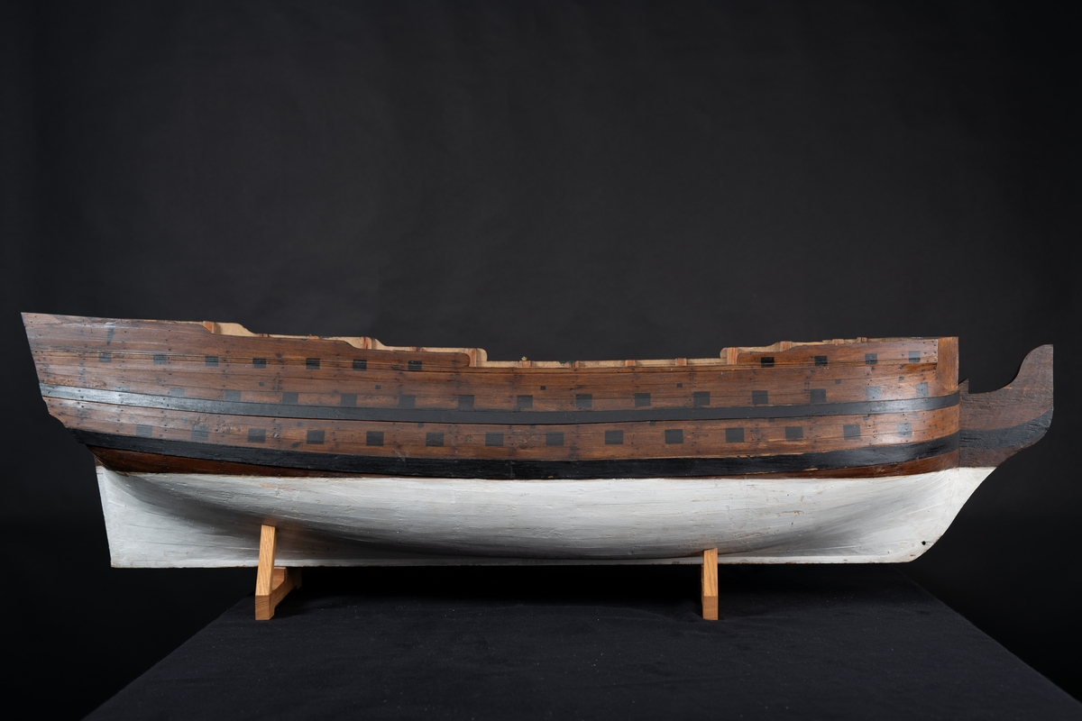 Fartygsmodell 80-kanonskepp efter 1765 års reglemente. Skrovmodell. Bordläggningen limmad på gavlar, utan inredning, galjon och akterspegel. Modellen brunmålad med svarta kanonportar och under vattenlinjen vitmålad.