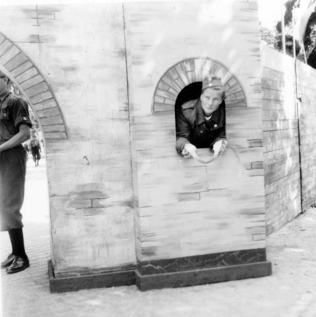 Barnens dag firande i Alingsås 1938. En tonårspojke i uniform och mössa står i ett fönster intill en port i muren och en tonårspojke i samma slags uniform står vid porten.