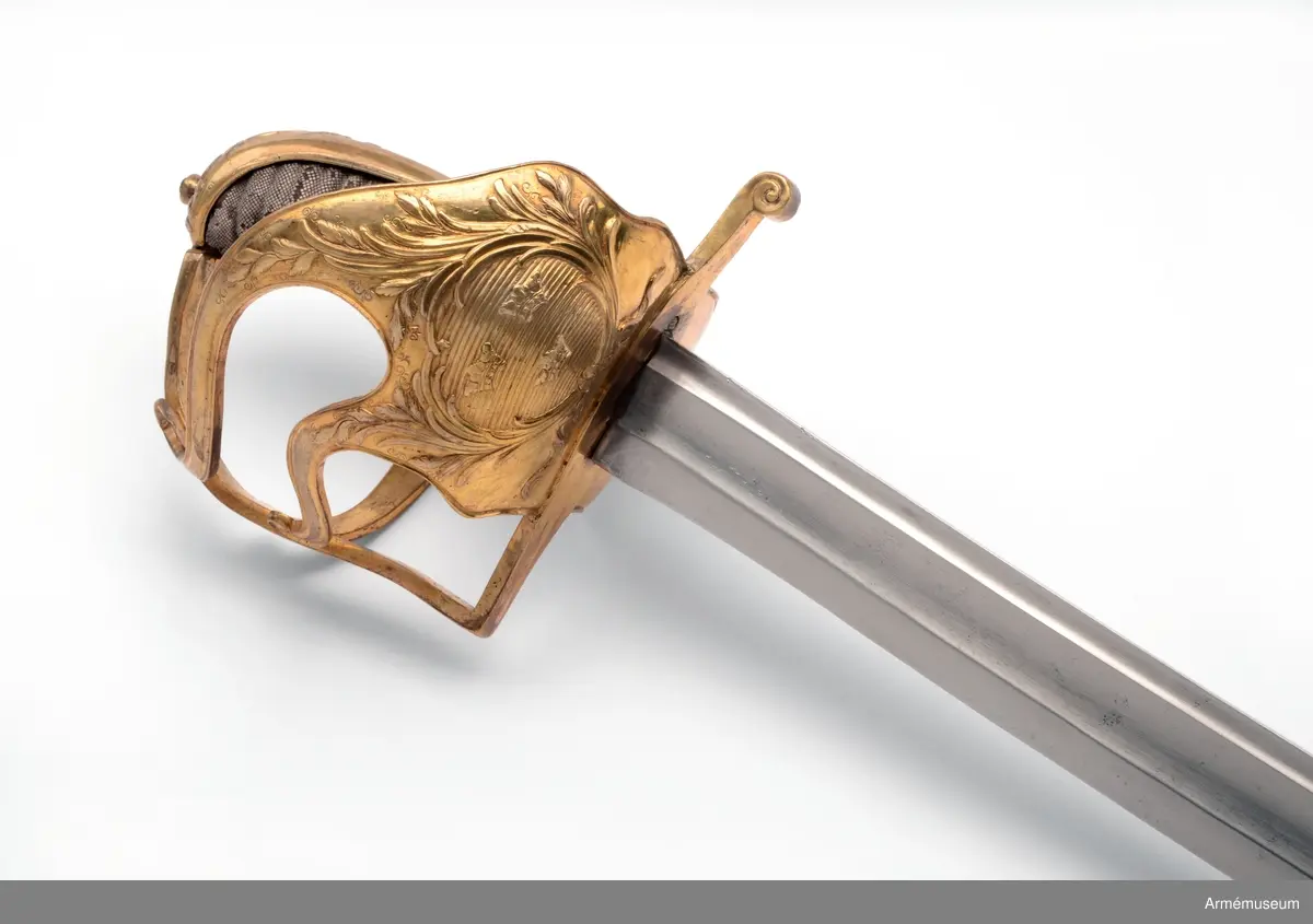 Sabeln är lik modellsabeln AM 36629, men avviker i frågan om fästets ornering. Den på kappan kring nitknappen anbringade ciselerade kransen är här större och går ned på ryggbeslaget och den på yttersidans parerplåt anbringade skölden med tre kronor är här större, ej krökt, nära nog cirkelrund och de sillerade palm- och lagerkvistar, som omger denna sköld, är här vida större och går in på ytterspängerna. Egendomligt nog finns såväl i Livrustkammaren som i ingenjör Orres samling sablar av denna typ, som på klingan har svenska riksvapnet med hessiska hjärtvapnet.