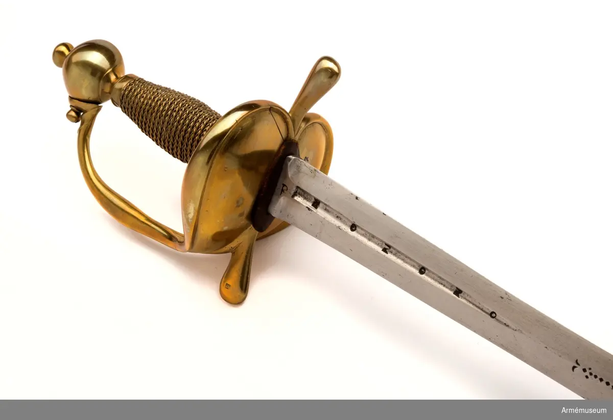 Klingan är tveeggad. Upptill på bägge sidor har den en omkring 140 mm lång blodrand. På yttersidan sitter dessutom en P-stämpel. Vid varje blodrands nedre ände finns ett delvis bortslipat, av prickar bestående ornament. Klingan är starkt avslipad, så att åsarna nedanför blodrandens slut nära nog förvandlats till ryggar. Fästet är av mässing och av drabanttyp. Knappen har formen av ett hoptryckt klot samt har rygg på fram- och baksidan. Knappens diameter är i sidled 37,5 mm, men över ryggarna 40,5 mm. Höjden är 33 mm. Upptill har knappen en stor nitknapp, som är instrypt. Nitknappens höjd är 16 mm, och diametern är 16 mm. Den har en spetsoval fot, som är 22 mm lång och 17 mm bred. Halsen är instrypt och 11 mm hög. Gränsen mellan nitknappen och knappen samt mellan knappen och halsen markeras genom en rand eller avsats. En dylik går även kring halsens nedre del. Knappen är rätt illa gjuten. Kaveln är spolformig, har fram och bak en flat rand, men sidorna är kullriga. Den har upp- och nedtill ett omkring 8 mm brett ringliknande beslag av mässingsbleck, varje beslag är prytt med två ränder samt är i övrigt lindat med två mässingstrådar, en grövre och en finare, vardera hopsnodd av två parter. Den ena tråden är höger-, den andra vänstersnodd. Parerstångens armar har spetsovalt tvärsnitt, är nedåtböjda samt blir mot de lindrigt avrundade ändarna tjockare och betydligt bredare. Den största tjockleken är för den främre armen 18,5 mm och för den bakre 18 mm. Avståndet mellan den främre eggen och  parerstångens framände är 54,5 mm. Mellan den bakre eggen och  bakänden är avståndet också 54,5 mm. Avståndet mellan klingans mitt och parerplåtens ytterkant är 52 mm, men mellan klingans  mitt och innerkanten 46 mm. Handbygeln är tjockast och bredast ungefär på mitten. Den har spetsovalt tvärsnitt och dess övre ände är fäst med en skruv vid knappen. På yttersidan av parerstångens främre arm finns en stämpel med bokstäver, sannolikt N. S.