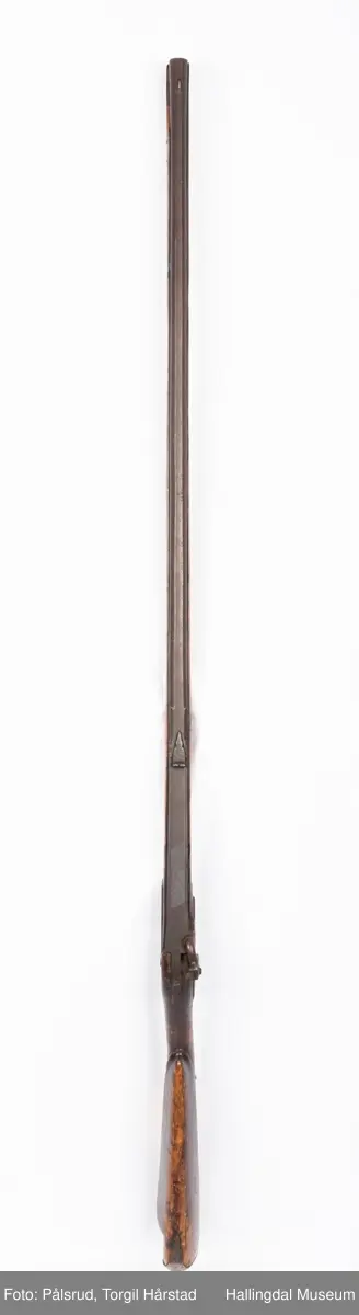 Gevær med perkusjonslås og kassepipe. Har mest sannsynlig vært ombygd fra flintlås. Geværet har kassepipe - har firkantet løp bakerst fra låsen til siktet midt på løpet. Fra låsen til siktet midt på løpet er løpet kasseformet og har en dekorert overgang til et svakt avrundet åttekantet løp. Det fremste siktet er av messing. Kolbekappen er festet med to skruer. Mangler avtrekksbøyle, reim og ladestokk. Montert på patentsvansskrue ved ombygging. Løpet er 15 cm i diameter og glattløpet.
