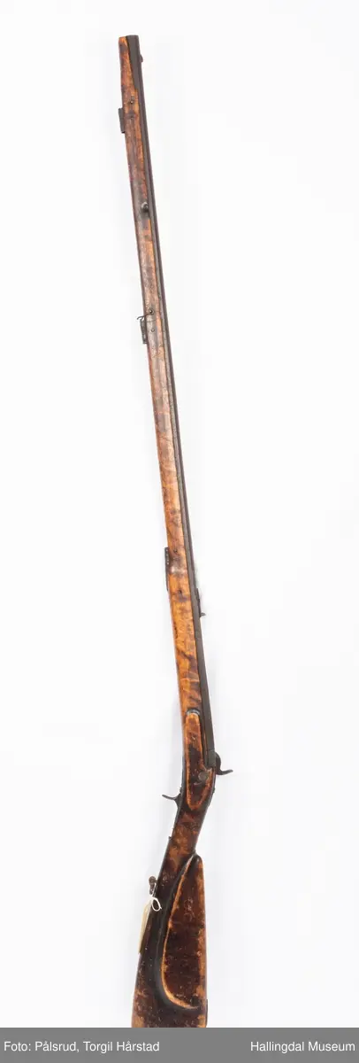 Gevær med perkusjonslås og kassepipe. Har mest sannsynlig vært ombygd fra flintlås. Geværet har kassepipe - har firkantet løp bakerst fra låsen til siktet midt på løpet. Fra låsen til siktet midt på løpet er løpet kasseformet og har en dekorert overgang til et svakt avrundet åttekantet løp. Det fremste siktet er av messing. Kolbekappen er festet med to skruer. Mangler avtrekksbøyle, reim og ladestokk. Montert på patentsvansskrue ved ombygging. Løpet er 15 cm i diameter og glattløpet.