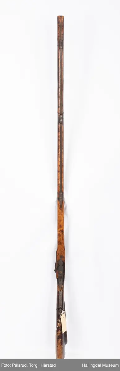 Gevær med perkusjonslås og kassepipe. Har mest sannsynlig vært ombygd fra flintlås. Geværet har kassepipe - har firkantet løp bakerst fra låsen til siktet midt på løpet. Fra låsen til siktet midt på løpet er løpet kasseformet og har en dekorert overgang til et svakt avrundet åttekantet løp. Det fremste siktet er av messing. Kolbekappen er festet med to skruer. Mangler avtrekksbøyle, reim og ladestokk. Montert på patentsvansskrue ved ombygging. Løpet er 15 cm i diameter og glattløpet.