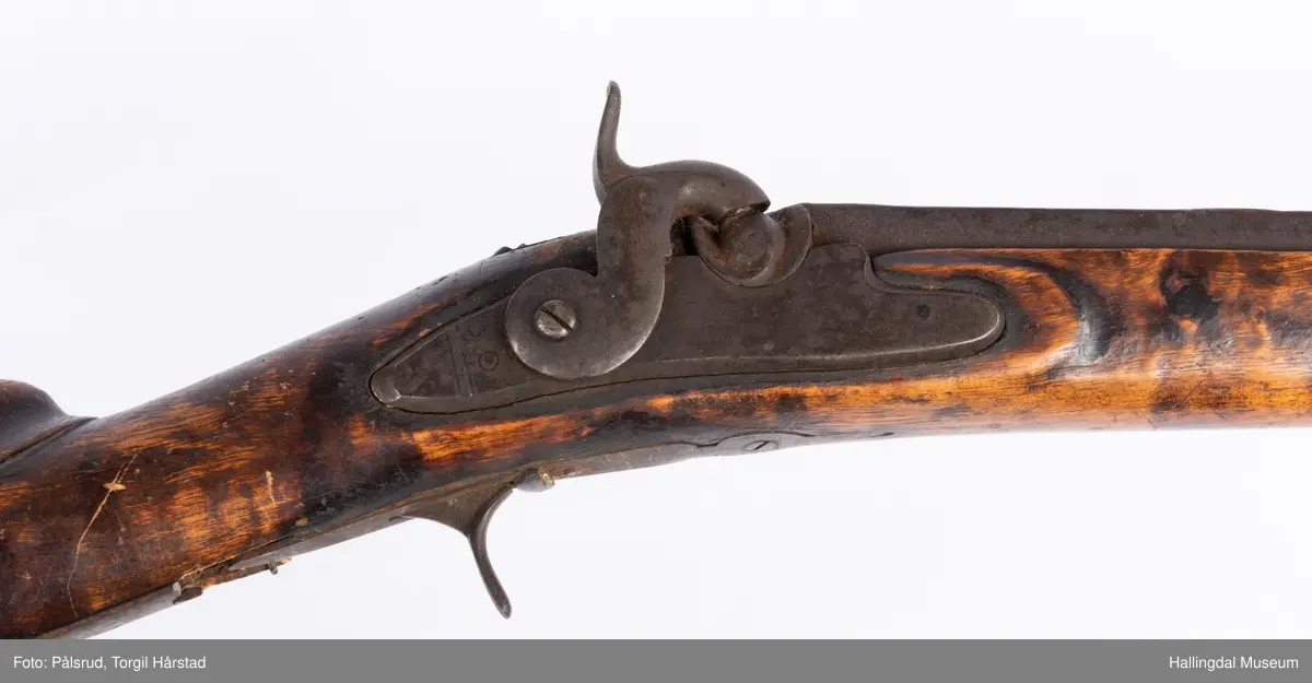 Gevær med perkusjonslås og kassepipe. Har mest sannsynlig vært ombygd fra flintlås. Geværet har kassepipe - har firkantet løp bakerst fra låsen til siktet midt på løpet. Fra låsen til siktet midt på løpet er løpet kasseformet og har en dekorert overgang til et svakt avrundet åttekantet løp. Det fremste siktet er av messing. Kolbekappen er festet med to skruer. Mangler avtrekksbøyle, reim og ladestokk. Montert på patentsvansskrue ved ombygging. Løpet er 15 cm i diameter og glattløpet.