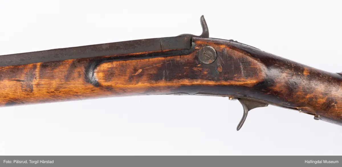 Gevær med perkusjonslås og kassepipe. Har mest sannsynlig vært ombygd fra flintlås. Geværet har kassepipe - har firkantet løp bakerst fra låsen til siktet midt på løpet. Fra låsen til siktet midt på løpet er løpet kasseformet og har en dekorert overgang til et svakt avrundet åttekantet løp. Det fremste siktet er av messing. Kolbekappen er festet med to skruer. Mangler avtrekksbøyle, reim og ladestokk. Montert på patentsvansskrue ved ombygging. Løpet er 15 cm i diameter og glattløpet.