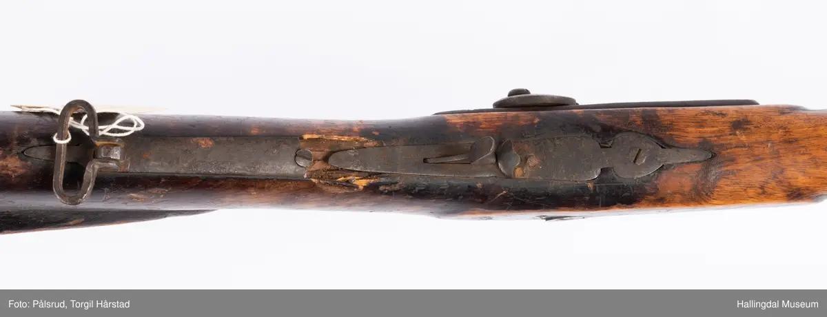 Gevær med perkusjonslås og kassepipe. Har mest sannsynlig vært ombygd fra flintlås. Geværet har kassepipe - har firkantet løp bakerst fra låsen til siktet midt på løpet. Fra låsen til siktet midt på løpet er løpet kasseformet og har en dekorert overgang til et svakt avrundet åttekantet løp. Det fremste siktet er av messing. Kolbekappen er festet med to skruer. Mangler avtrekksbøyle, reim og ladestokk. Montert på patentsvansskrue ved ombygging. Løpet er 15 cm i diameter og glattløpet.