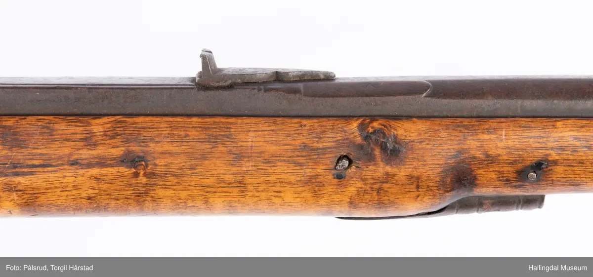 Gevær med perkusjonslås og kassepipe. Har mest sannsynlig vært ombygd fra flintlås. Geværet har kassepipe - har firkantet løp bakerst fra låsen til siktet midt på løpet. Fra låsen til siktet midt på løpet er løpet kasseformet og har en dekorert overgang til et svakt avrundet åttekantet løp. Det fremste siktet er av messing. Kolbekappen er festet med to skruer. Mangler avtrekksbøyle, reim og ladestokk. Montert på patentsvansskrue ved ombygging. Løpet er 15 cm i diameter og glattløpet.